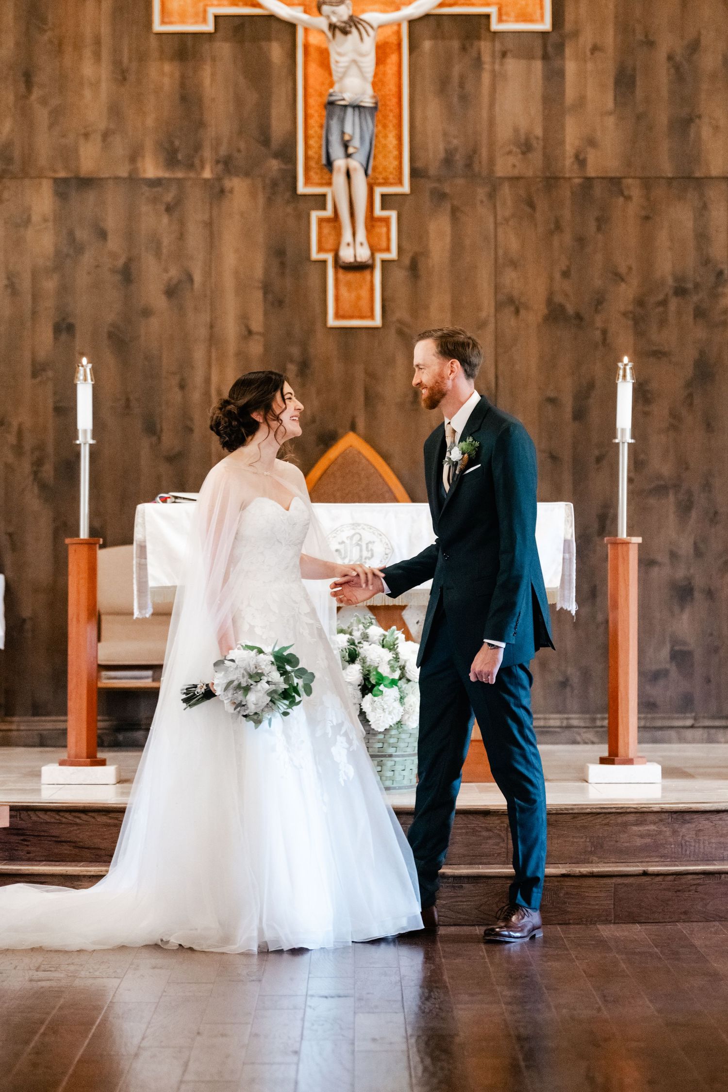 A couple shares their first look in a church with wooden walls and orange cross decor.