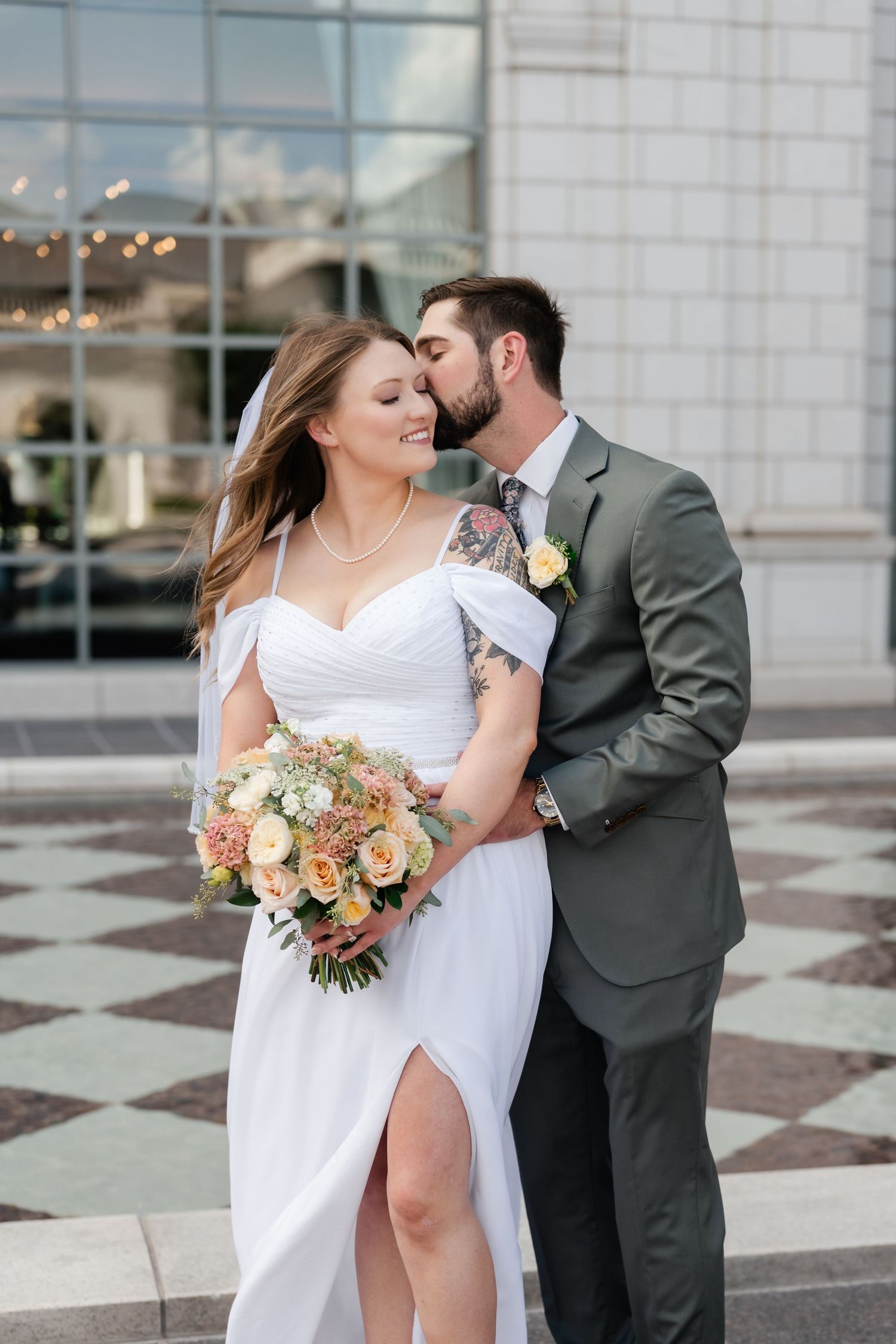 A couple shares a romantic kiss during their wedding photoshoot on a checkered plaza.