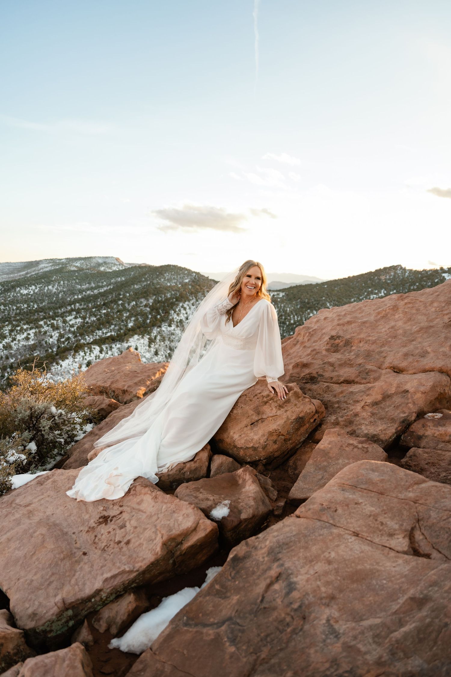 Elegant bridal portraits on dramatic red rock formations with snow-capped mountains in the distance.