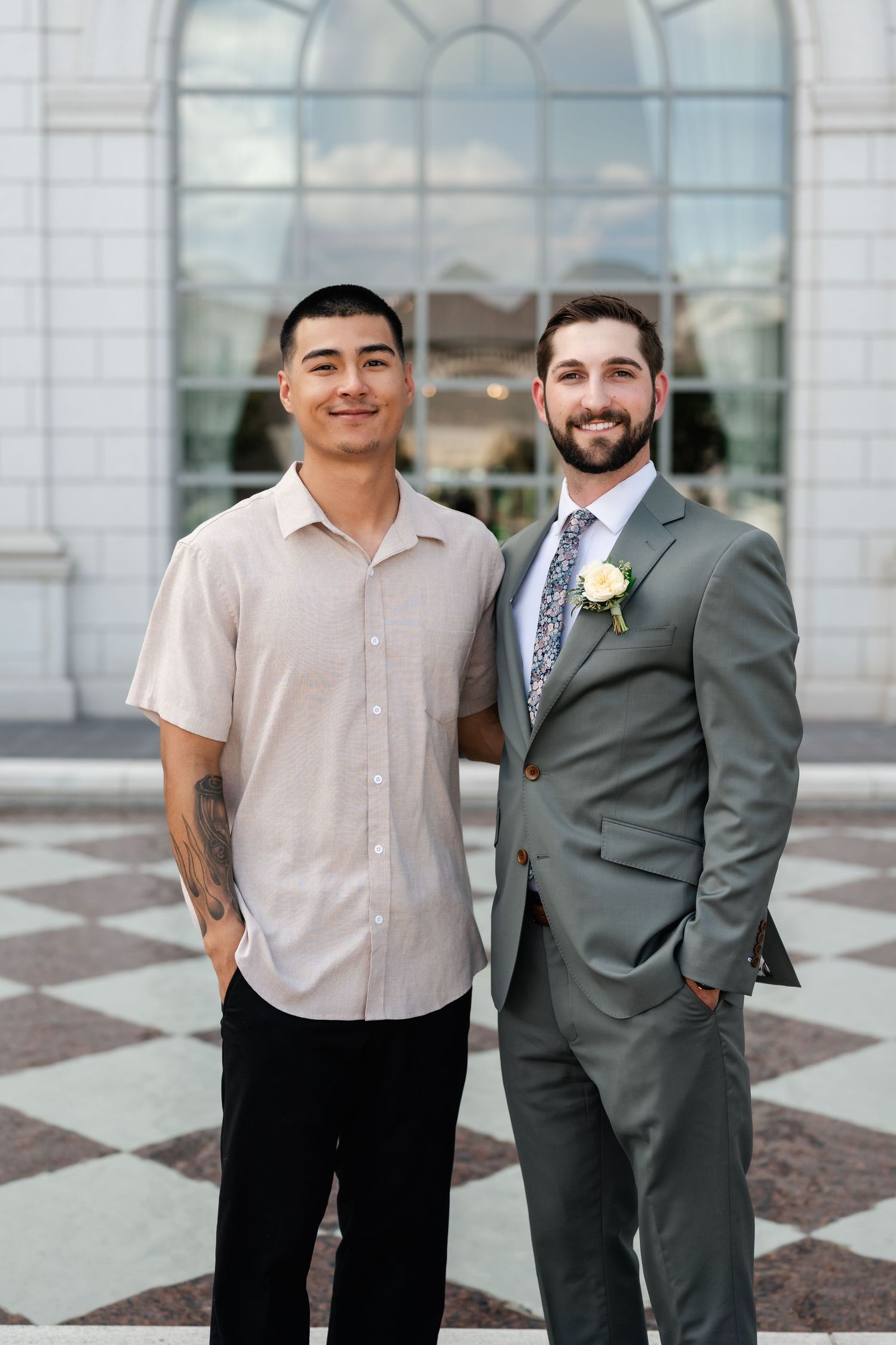 Two people stand together in front of a grand building with glass windows and stone architecture.