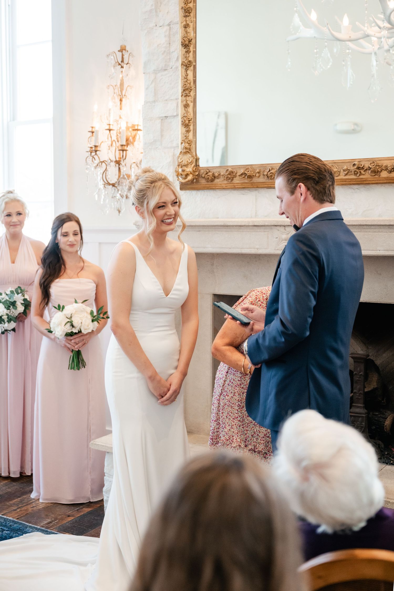 Intimate wedding ceremony taking place in bright room with ornate gold mirror and chandelier.