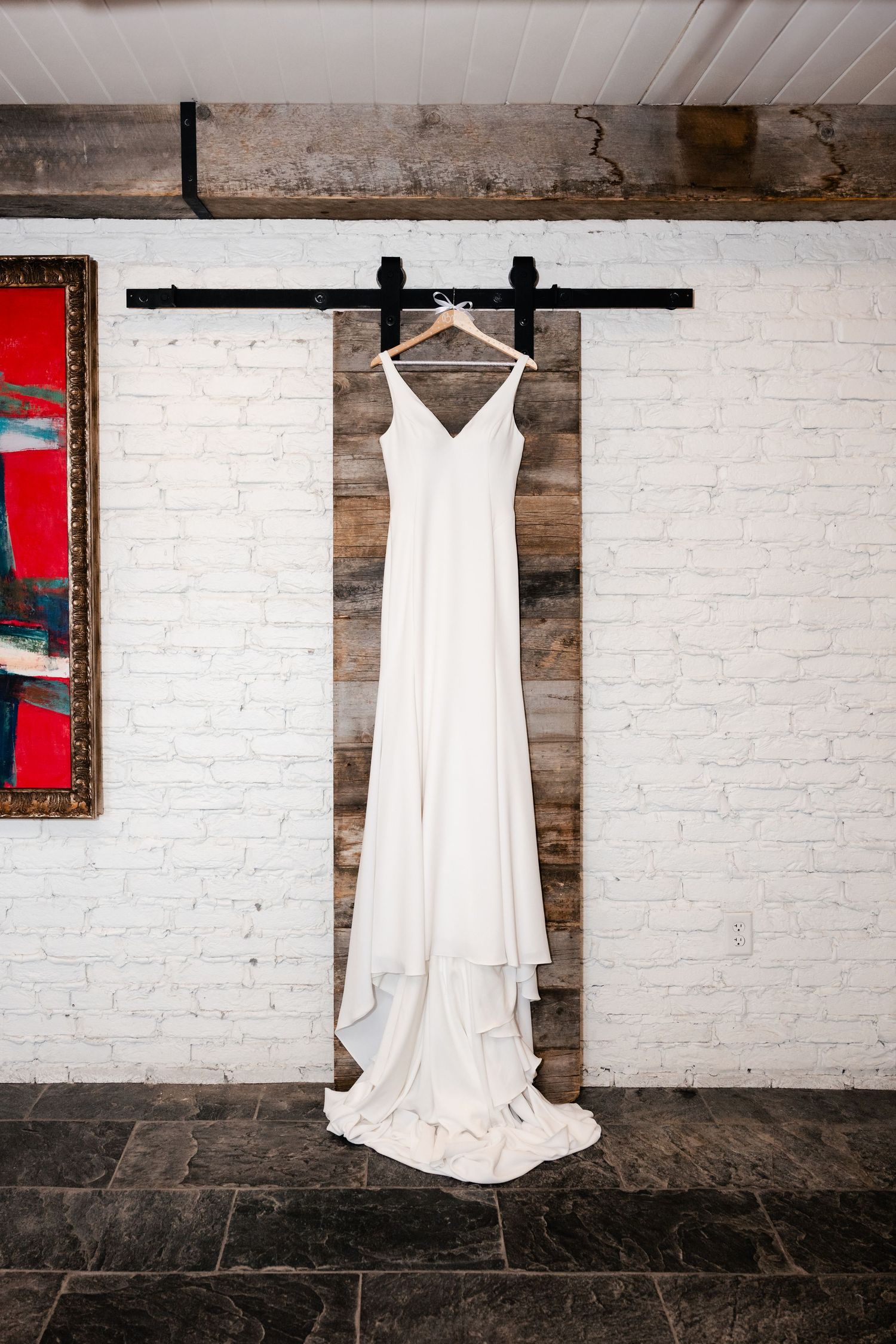 White wedding dress hanging against exposed brick wall with industrial decor elements.