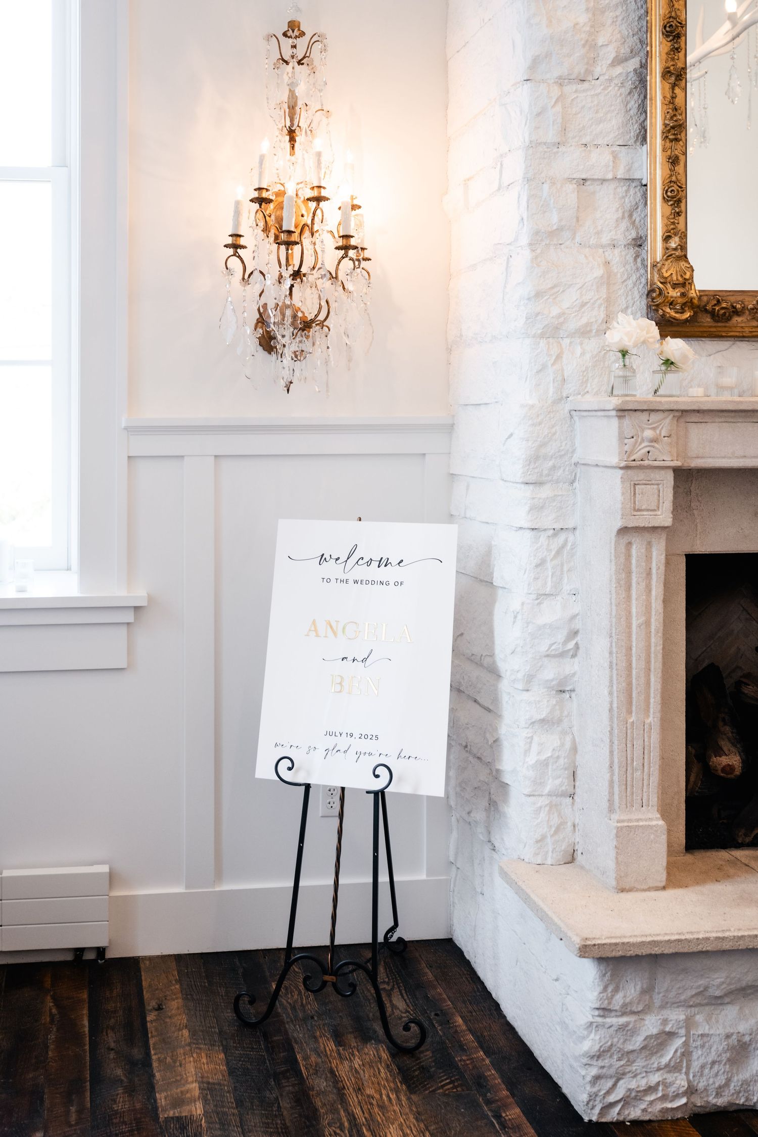 White welcome sign on easel stand against white brick wall with crystal chandelier.
