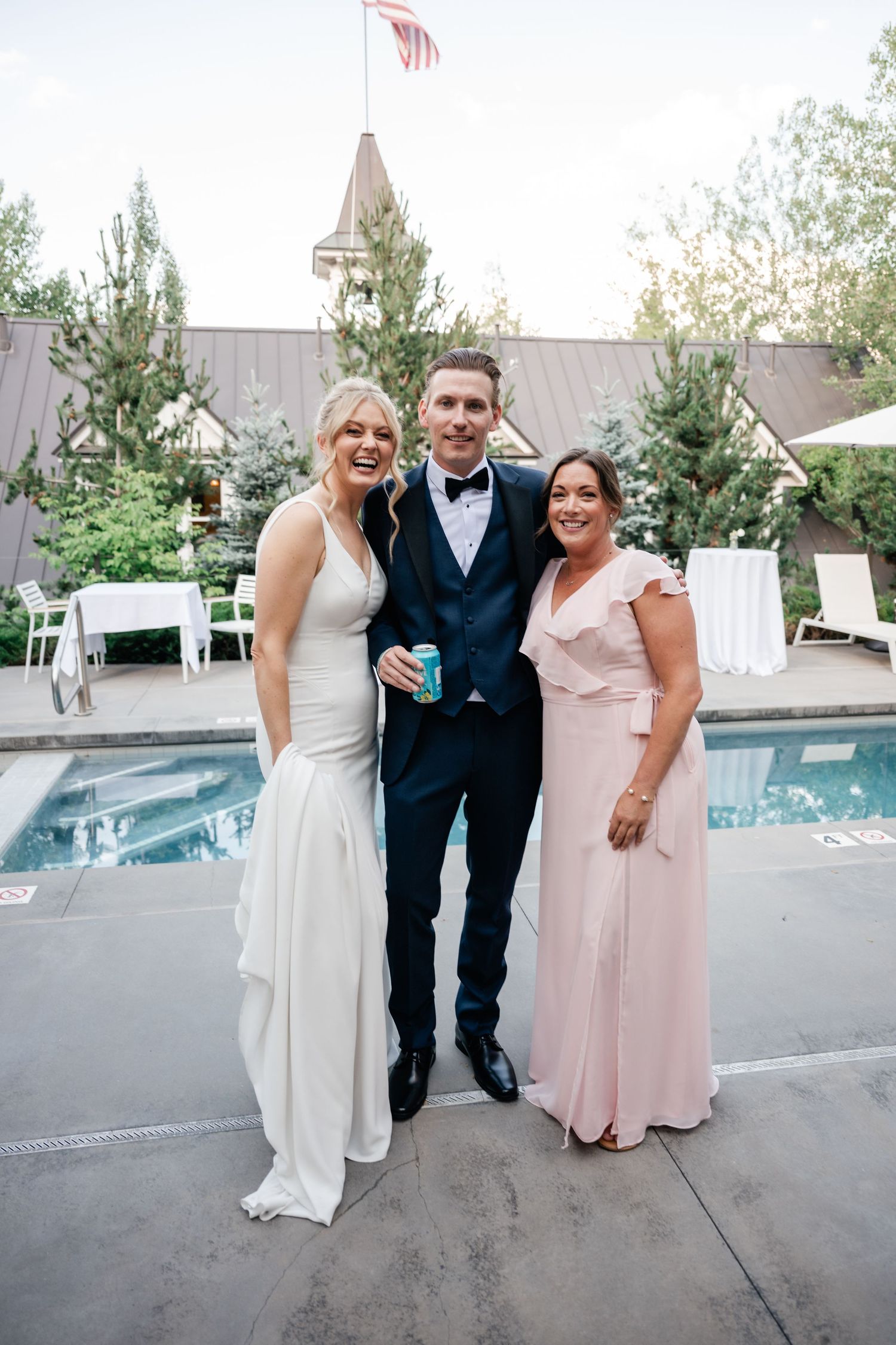 Wedding party members share laughs on a patio with a swimming pool in the background.
