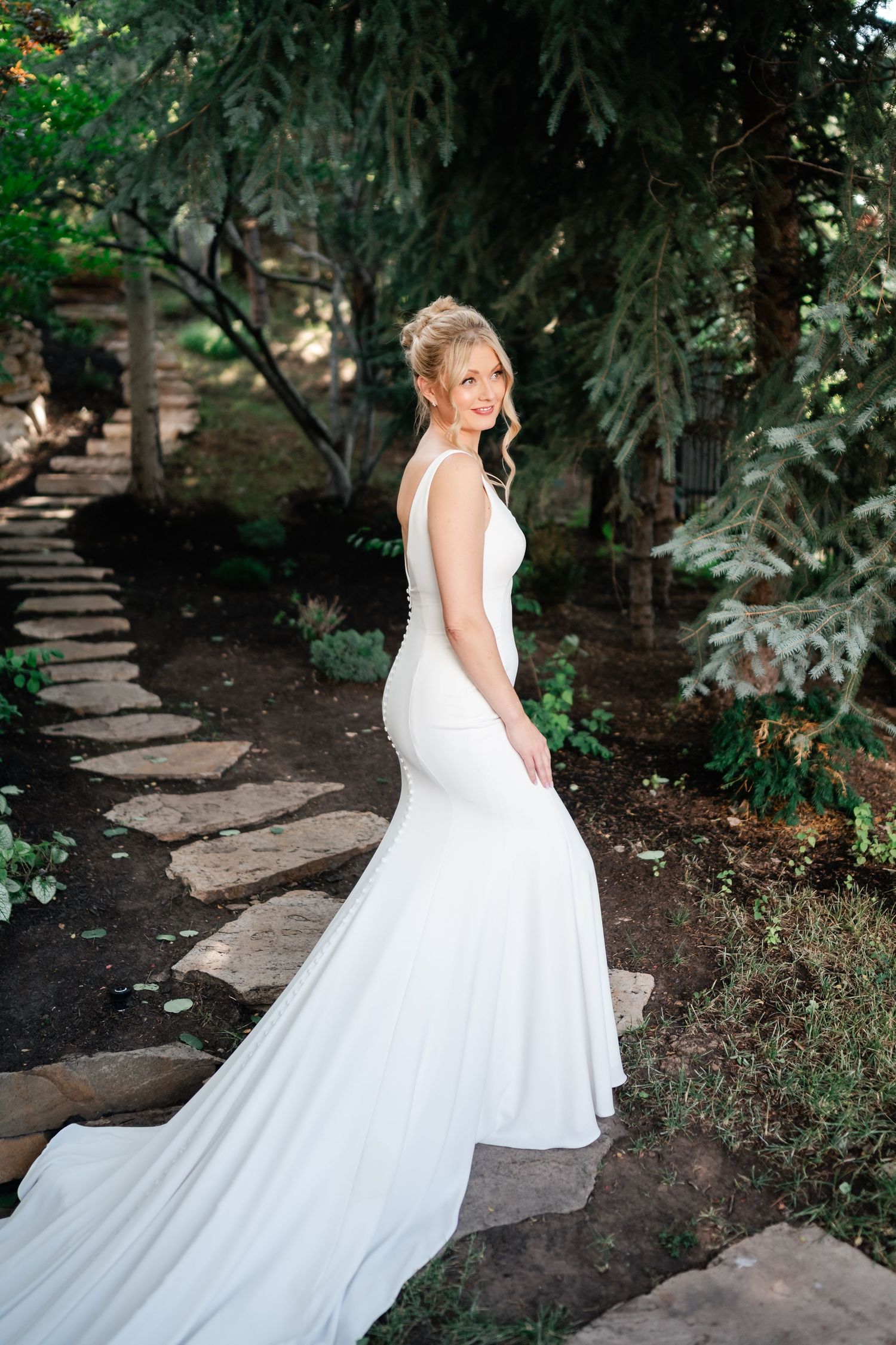 A flowing white wedding dress cascades down stone garden steps surrounded by lush greenery.