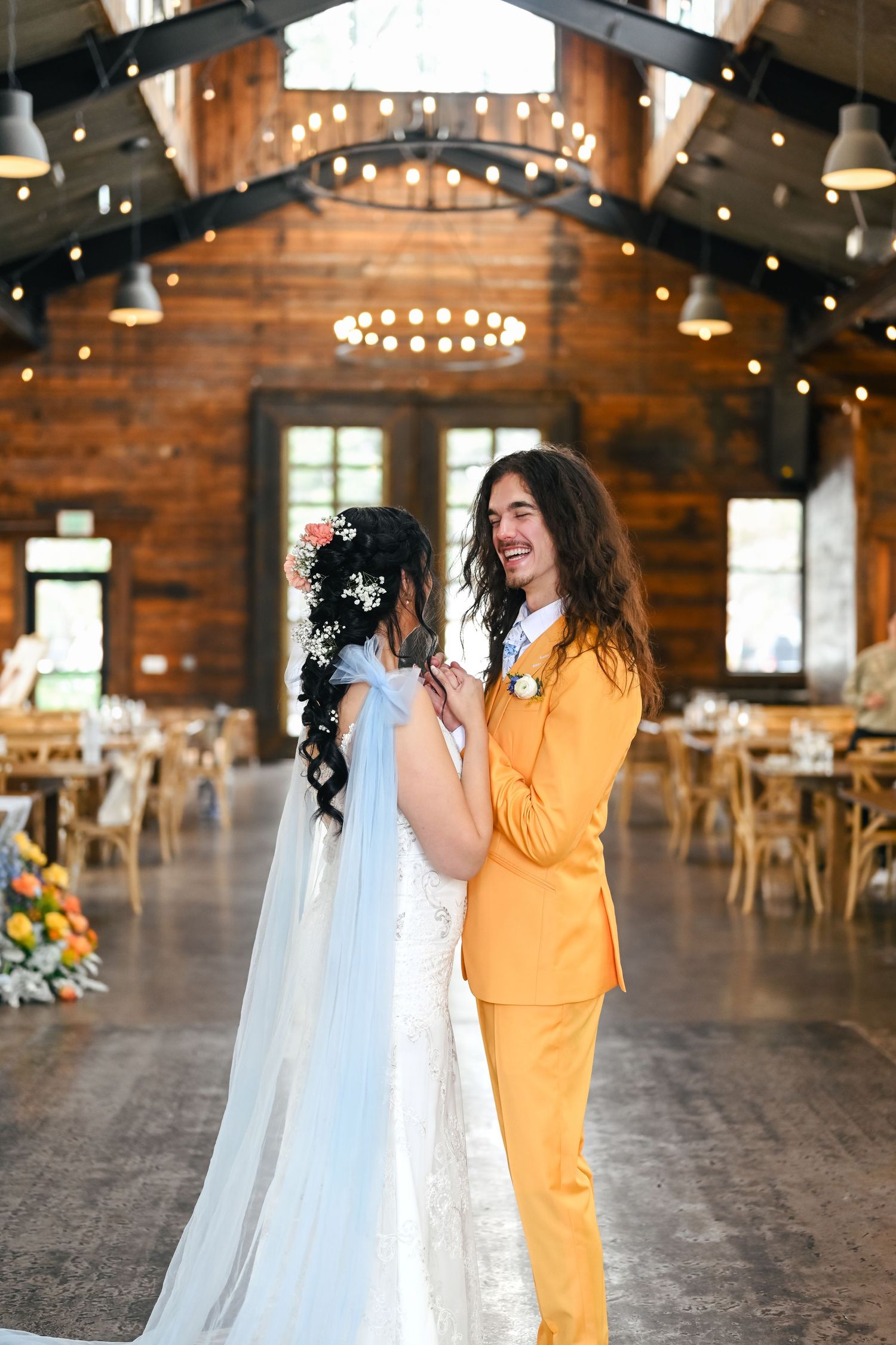 A couple shares a joyful moment in a rustic barn venue decorated with string lights for their wedding celebration. Knot & Pine photographer.