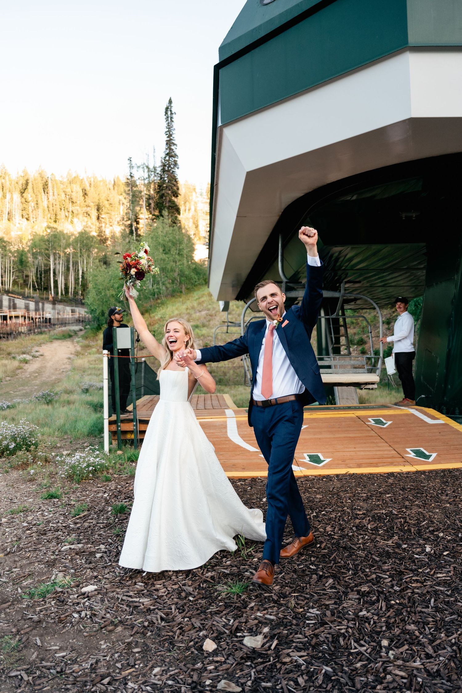 A celebratory moment of joy at an outdoor mountain venue with evergreen trees and ski lifts in the background. Park City Wedding Photos.