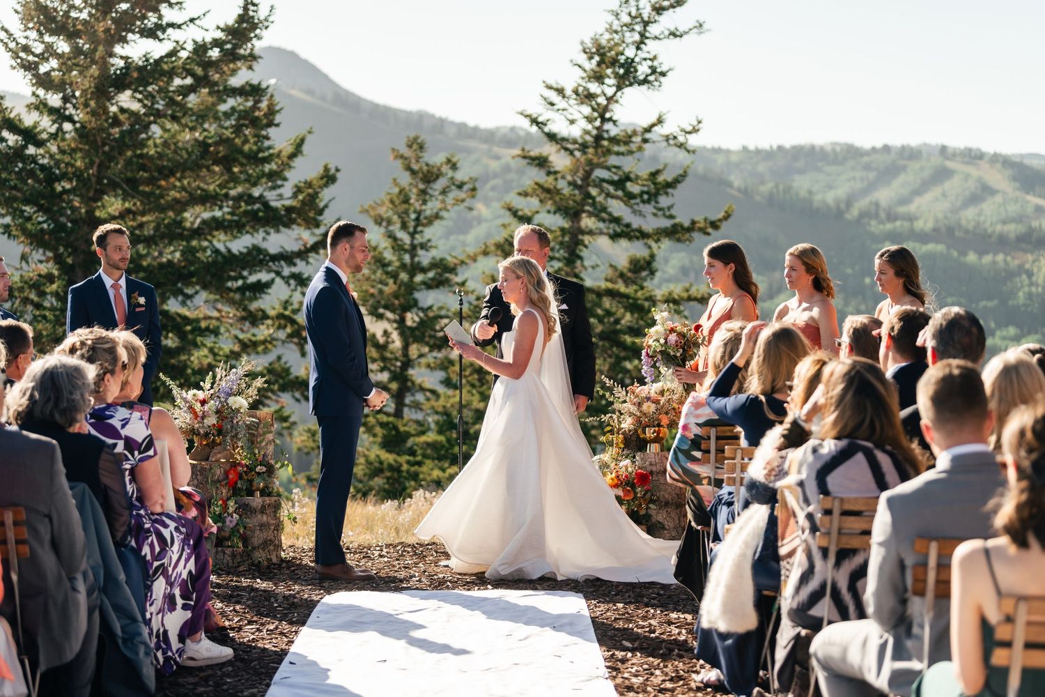 An outdoor mountain wedding ceremony takes place with evergreen trees and scenic mountain views in the background. Park City Wedding Photo.