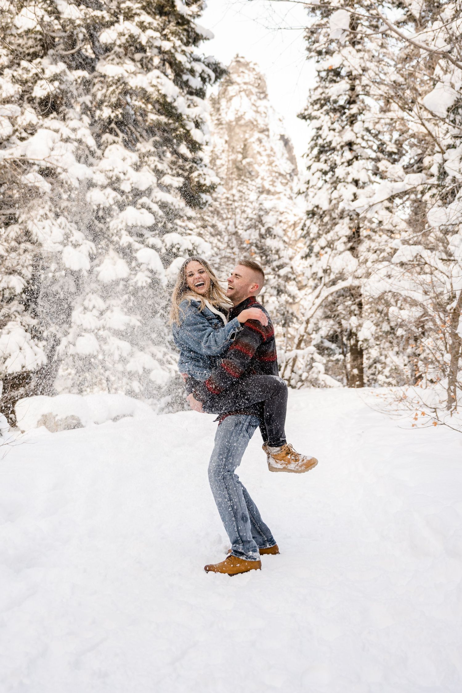 A playful moment captured in the snow as they embrace surrounded by snow-covered trees.