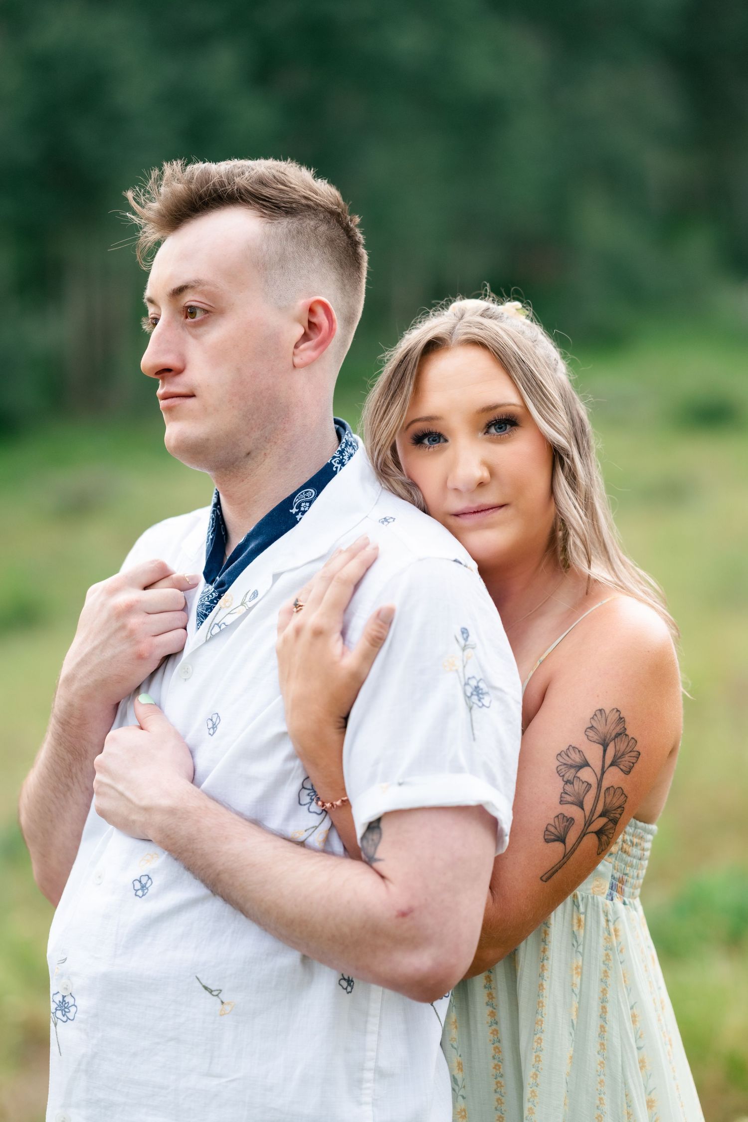 A couple in an outdoor setting, with him in a white patterned shirt and her in a yellow dress embracing from behind. Guardsman Pass Session.