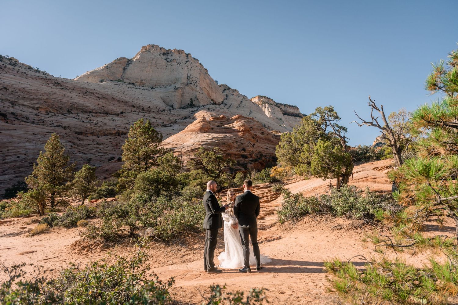 A wedding ceremony takes place on a trail with majestic desert cliffs in the background.