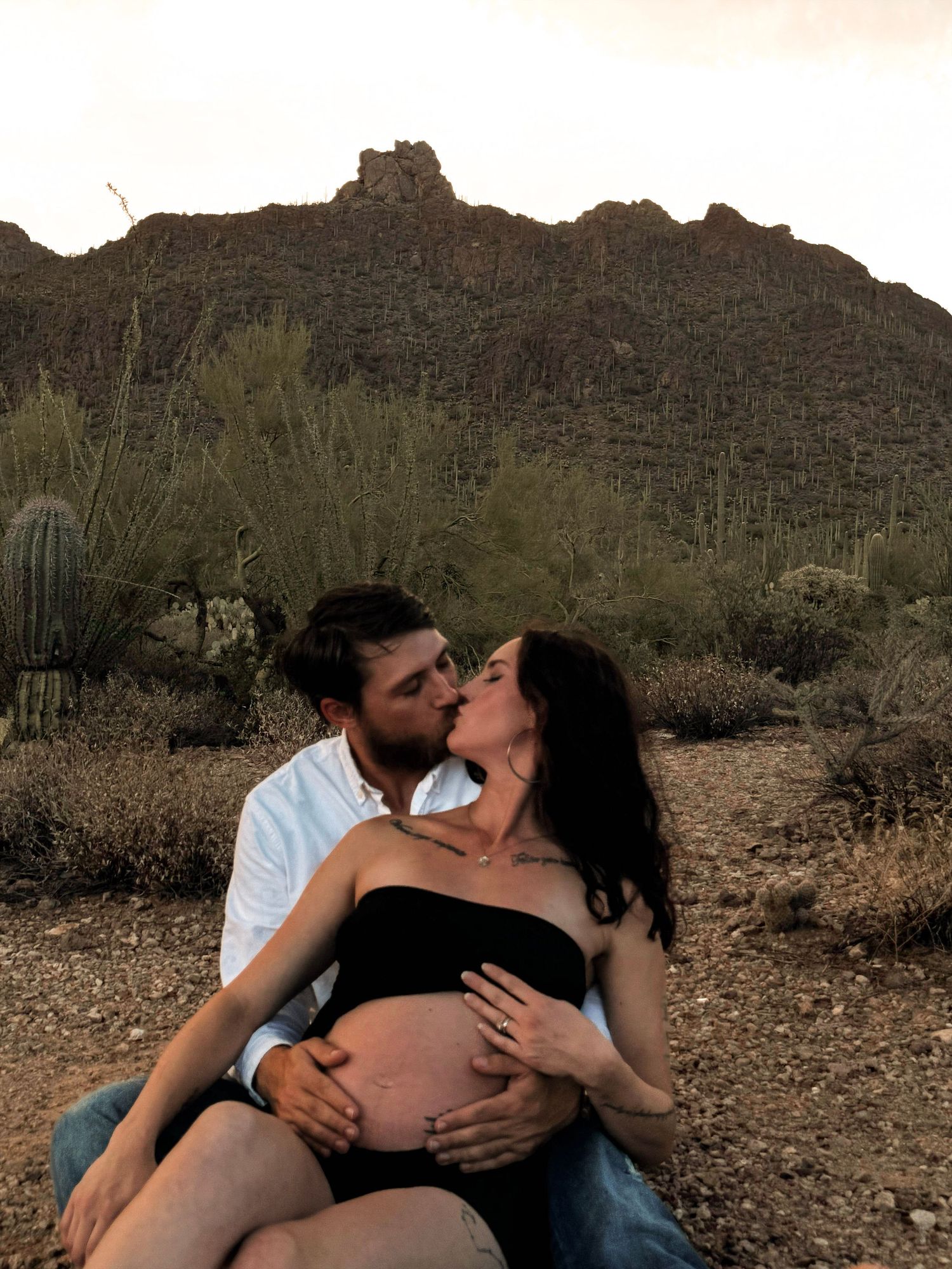Intimate maternity photo session against desert mountain backdrop at sunset.