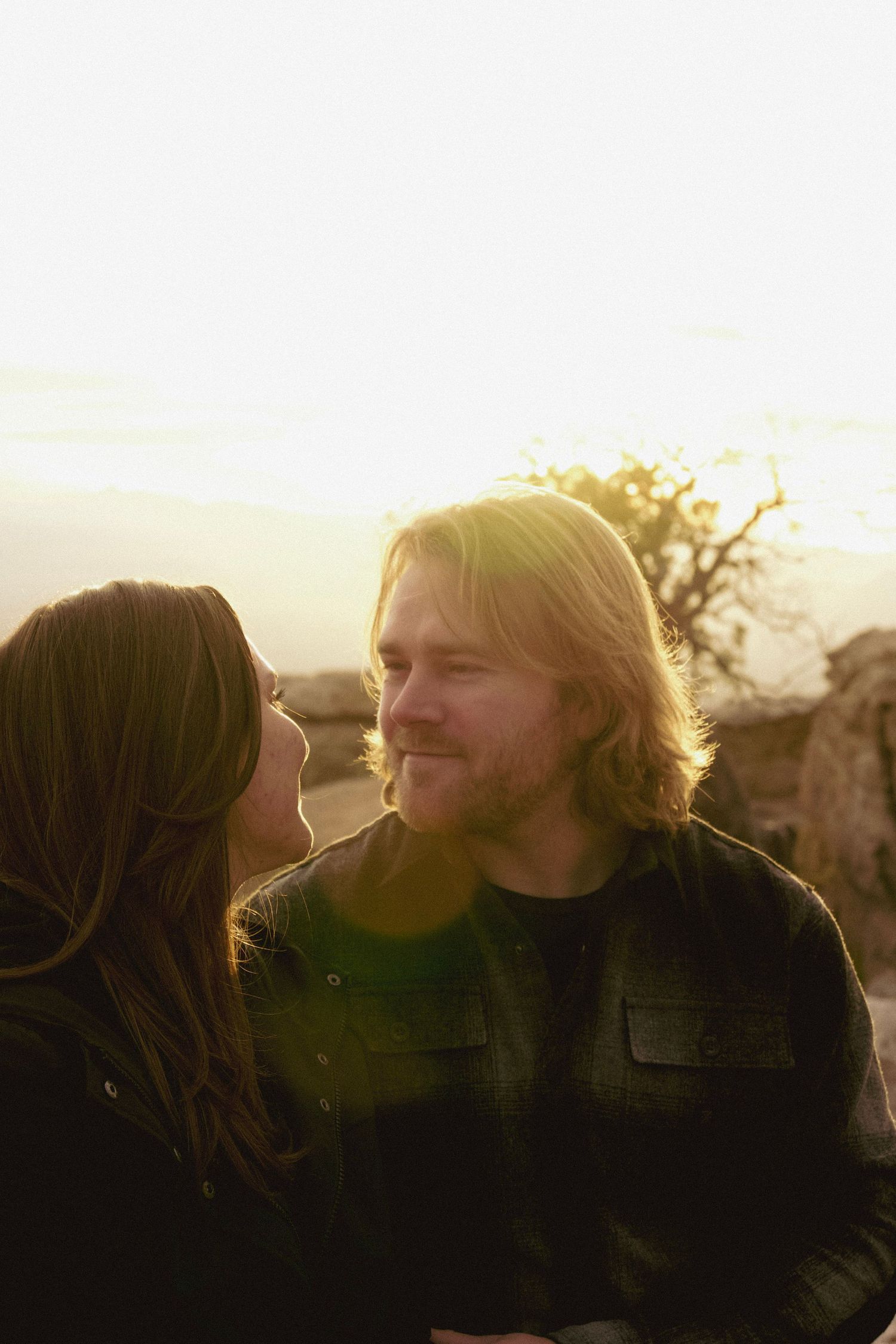 A couple shares a tender moment during sunset with golden light illuminating their profiles.