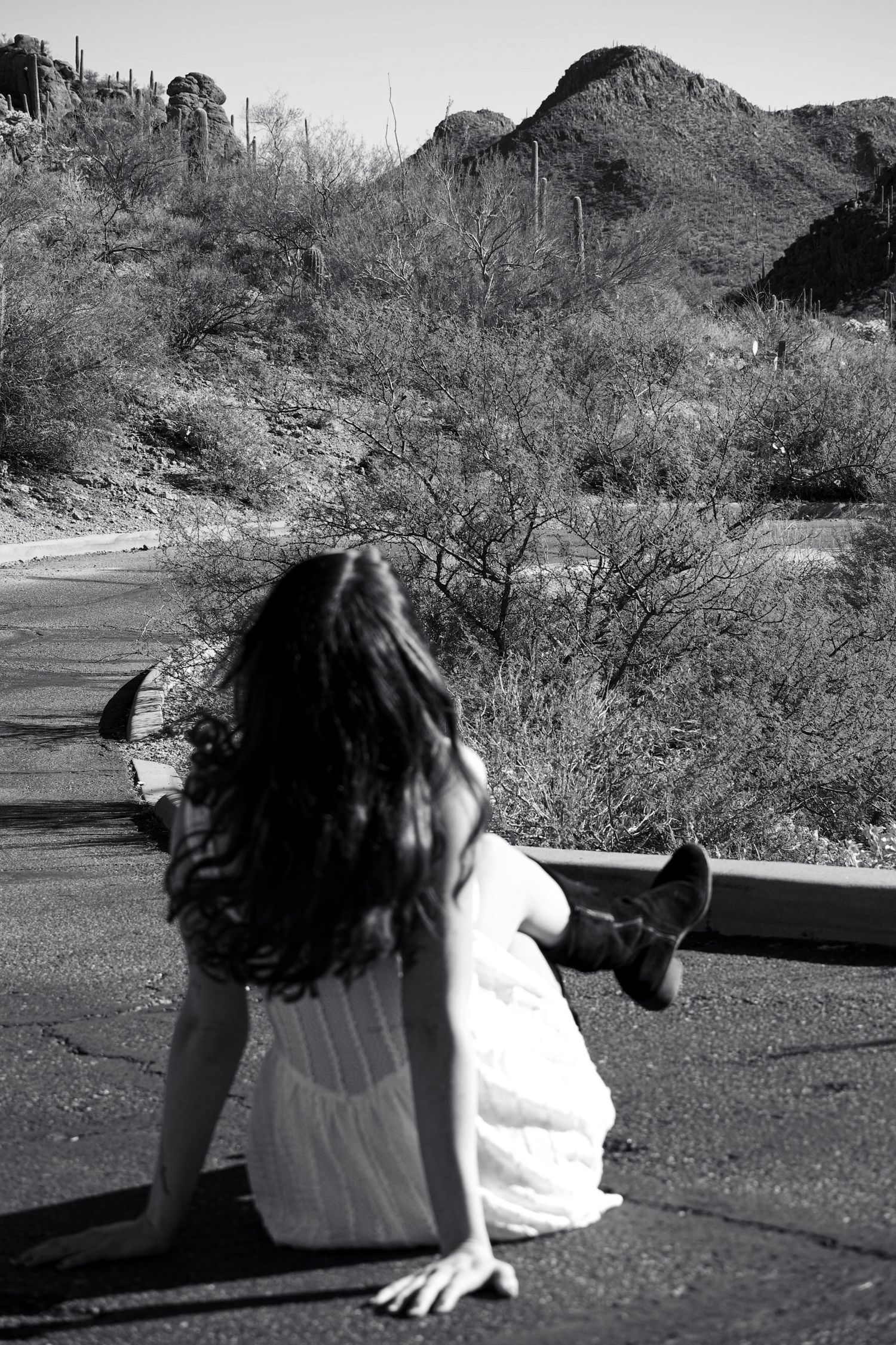 A figure in white lies on desert ground against a backdrop of rugged mountain terrain.