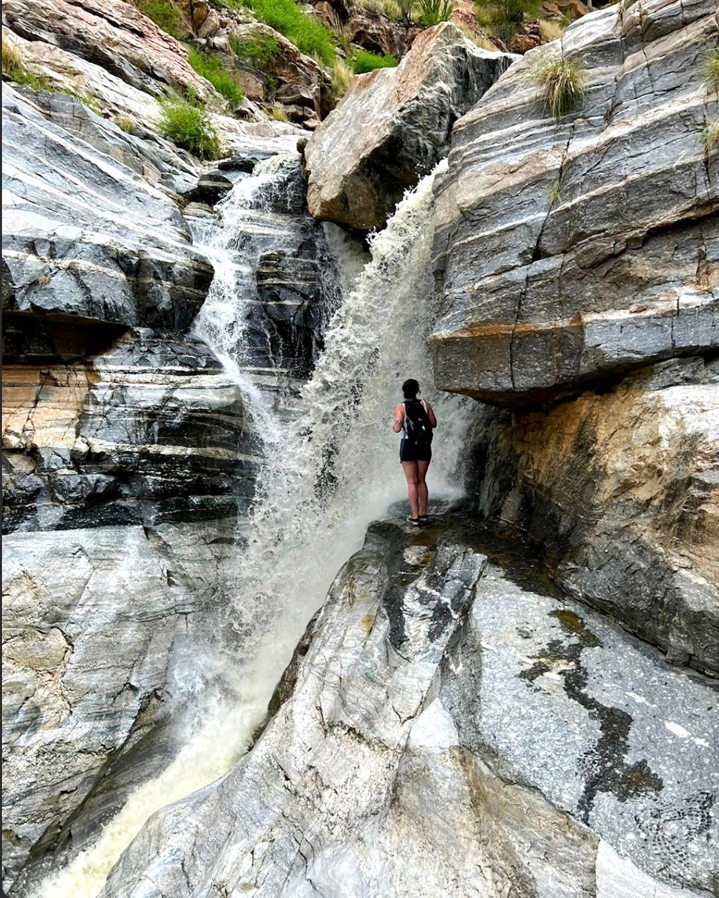 Rock climber scaling a steep granite wall with a cascading waterfall in the background at a scenic mountain location.
