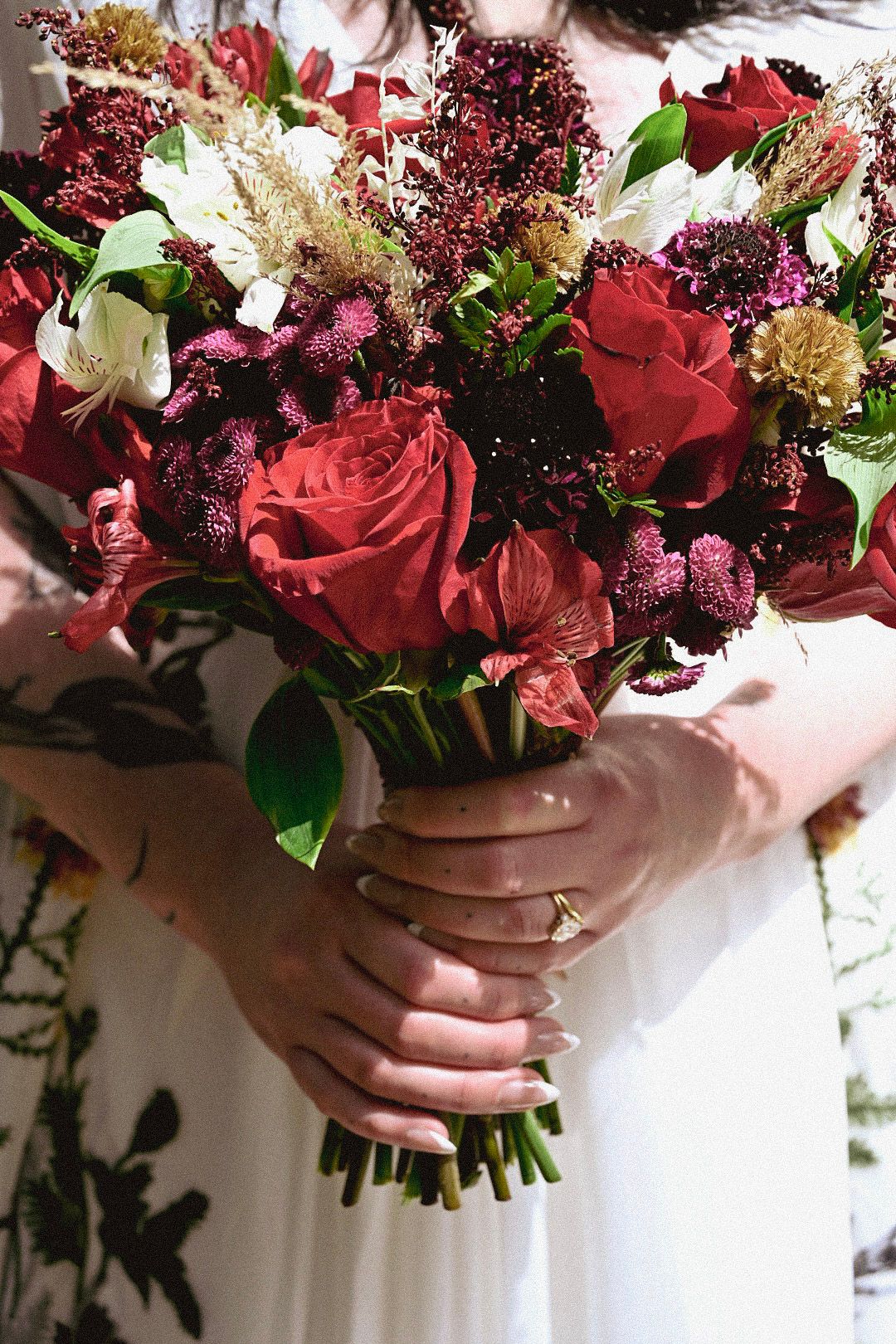 A beautiful bouquet of red roses and mixed flowers being held against a white background.