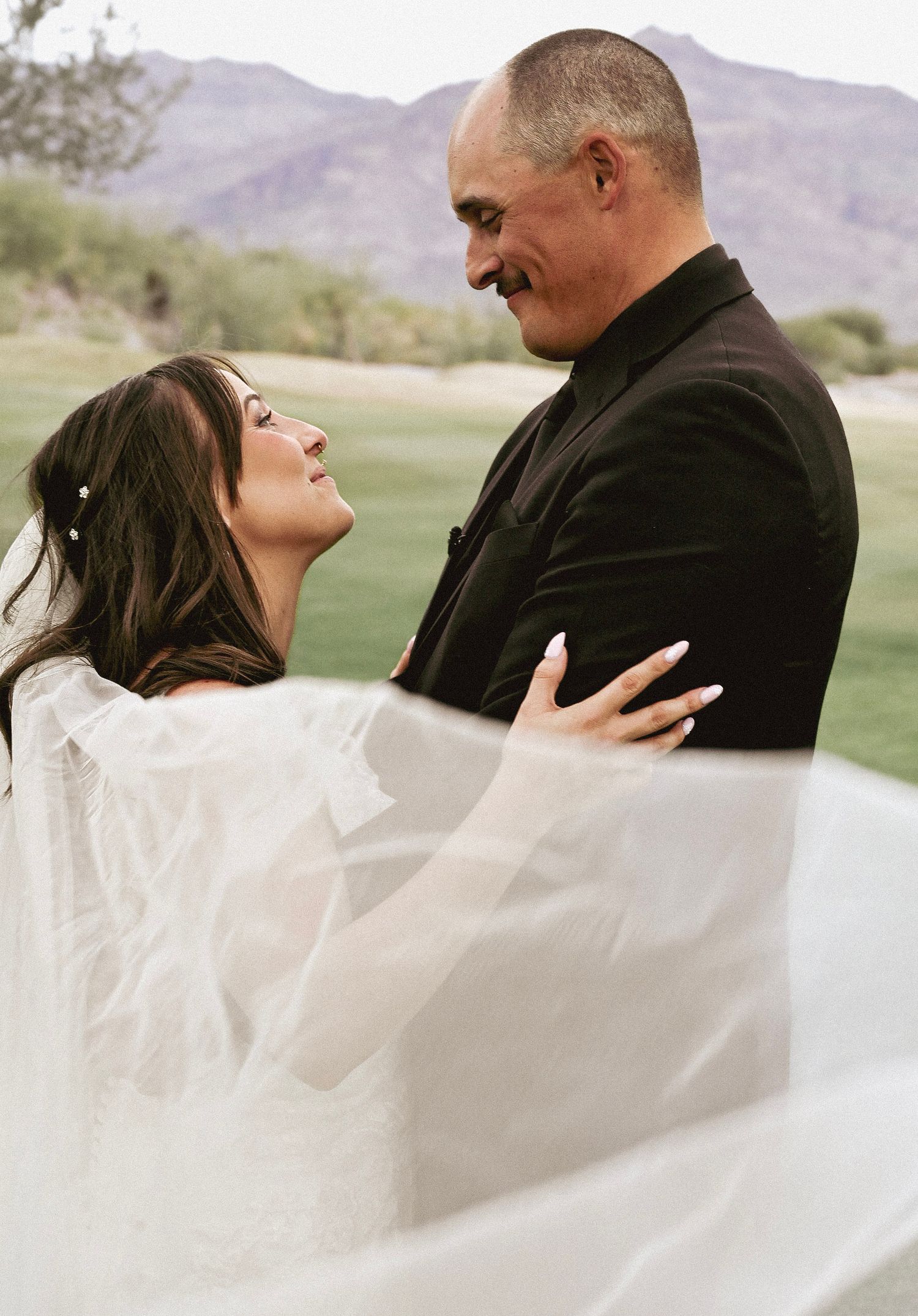 A series of romantic wedding photos showing a couple embracing outdoors with flowing white veil and mountains in background.