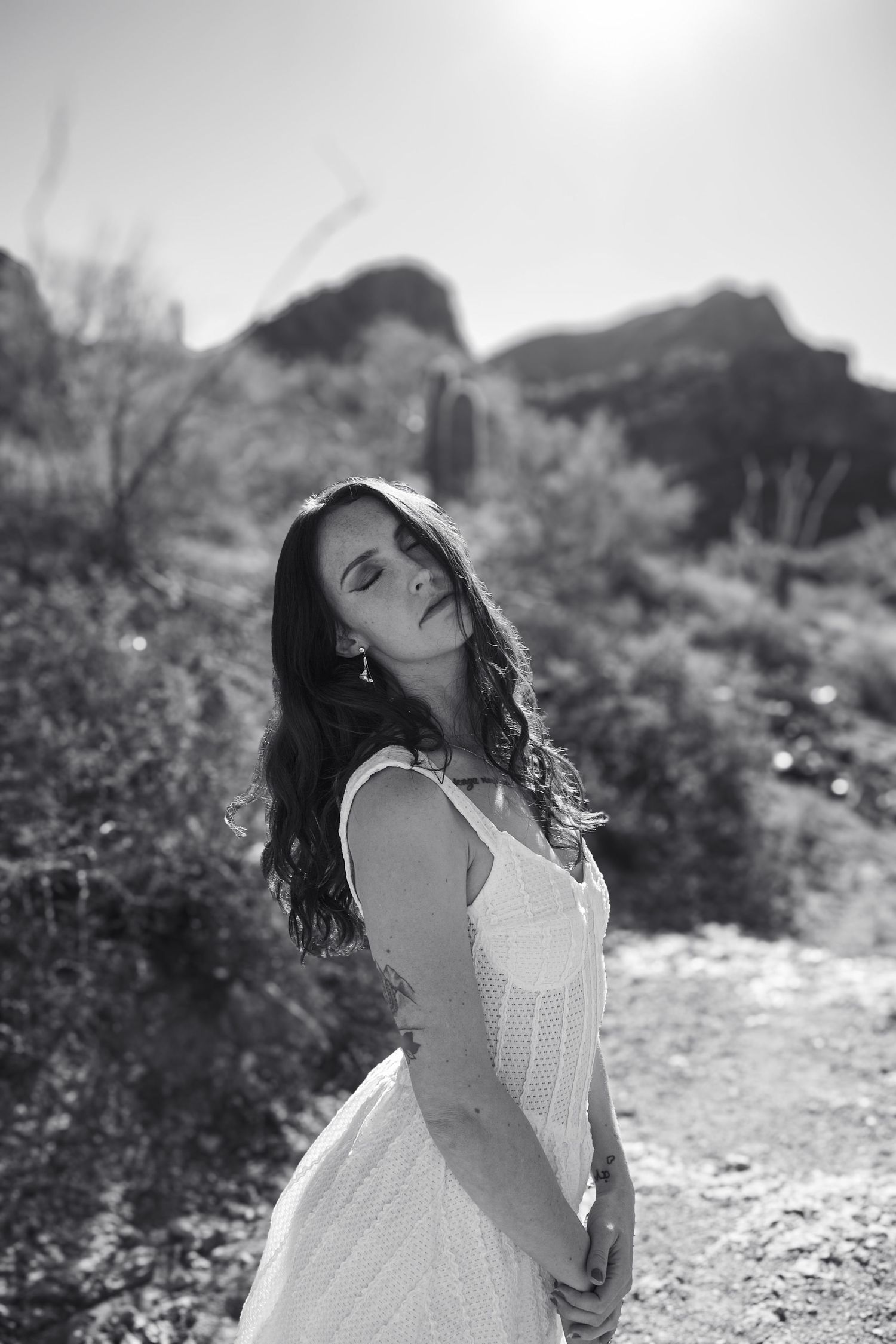 Woman in white dress posing against desert mountain landscape in soft light.