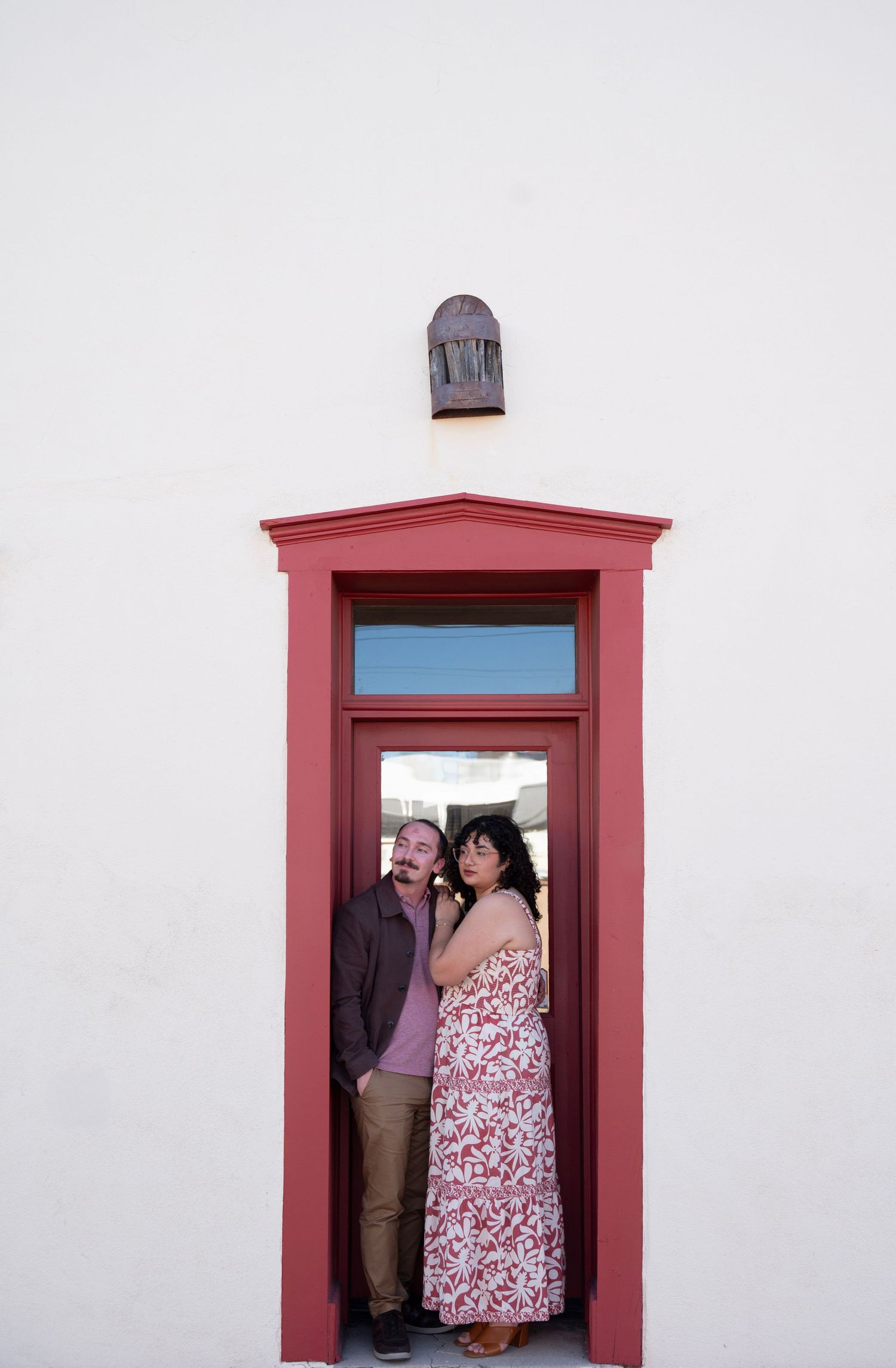 Three sequential photos show a couple sharing an intimate moment through a red-framed doorway against a white wall.