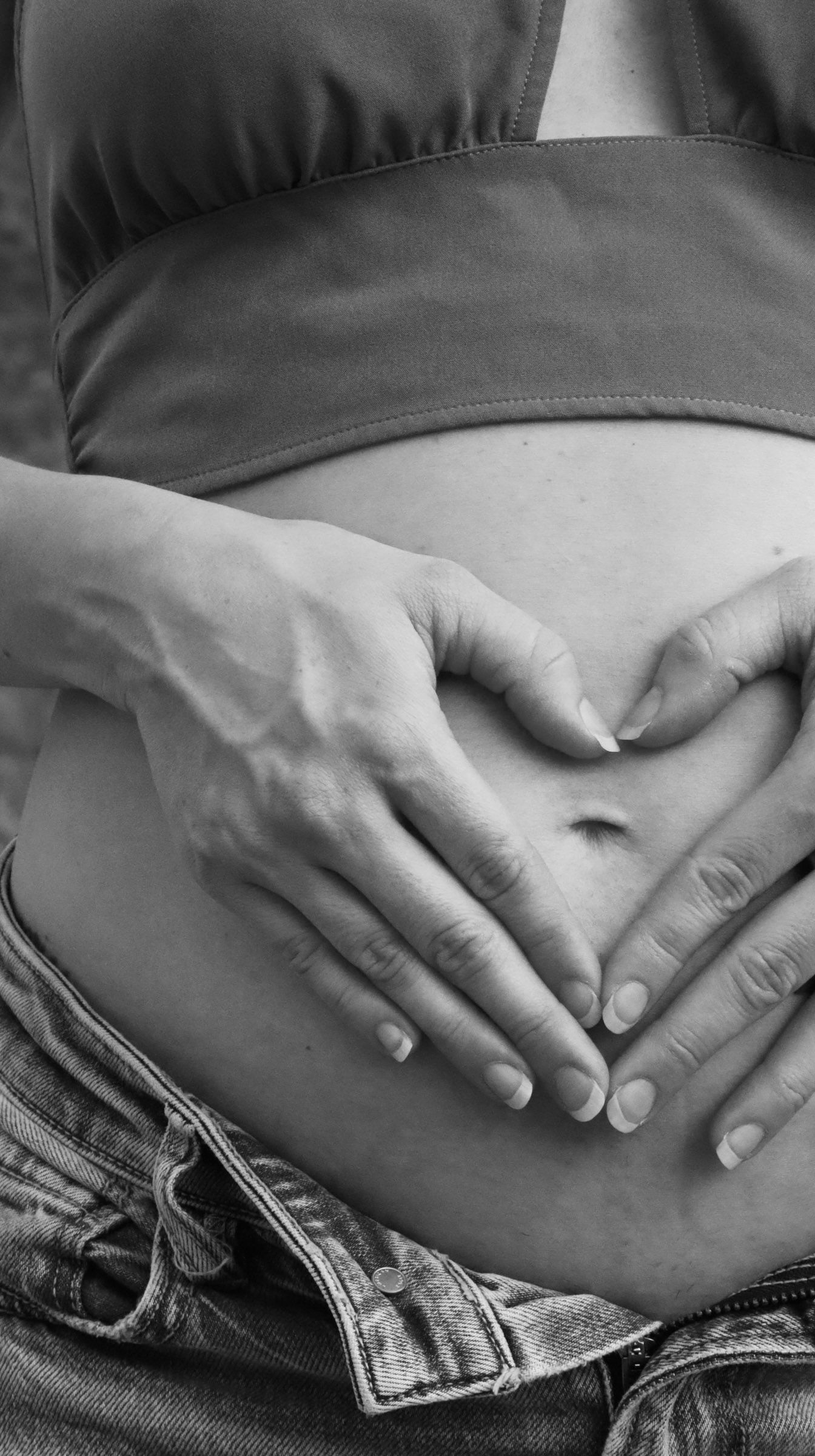 Close-up black and white photo of hands resting gently on a pregnant belly.