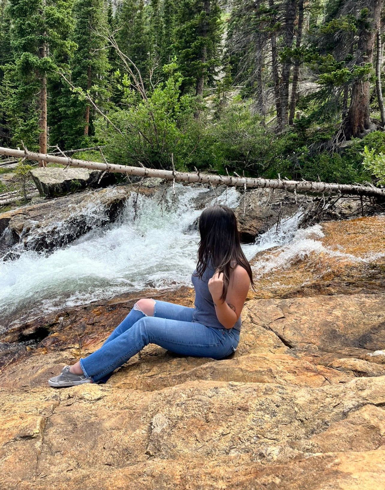 A person lying on their stomach on a rocky ledge near a rushing waterfall in a forest setting.