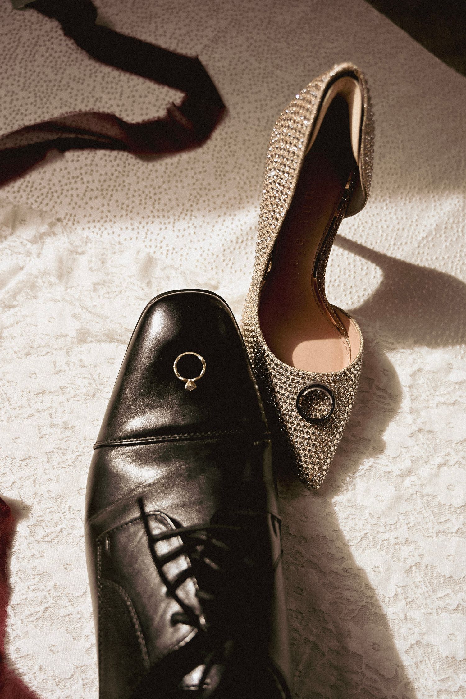 A formal black leather men's dress shoe paired with a sparkly rhinestone-covered women's high heel pump on white fabric.