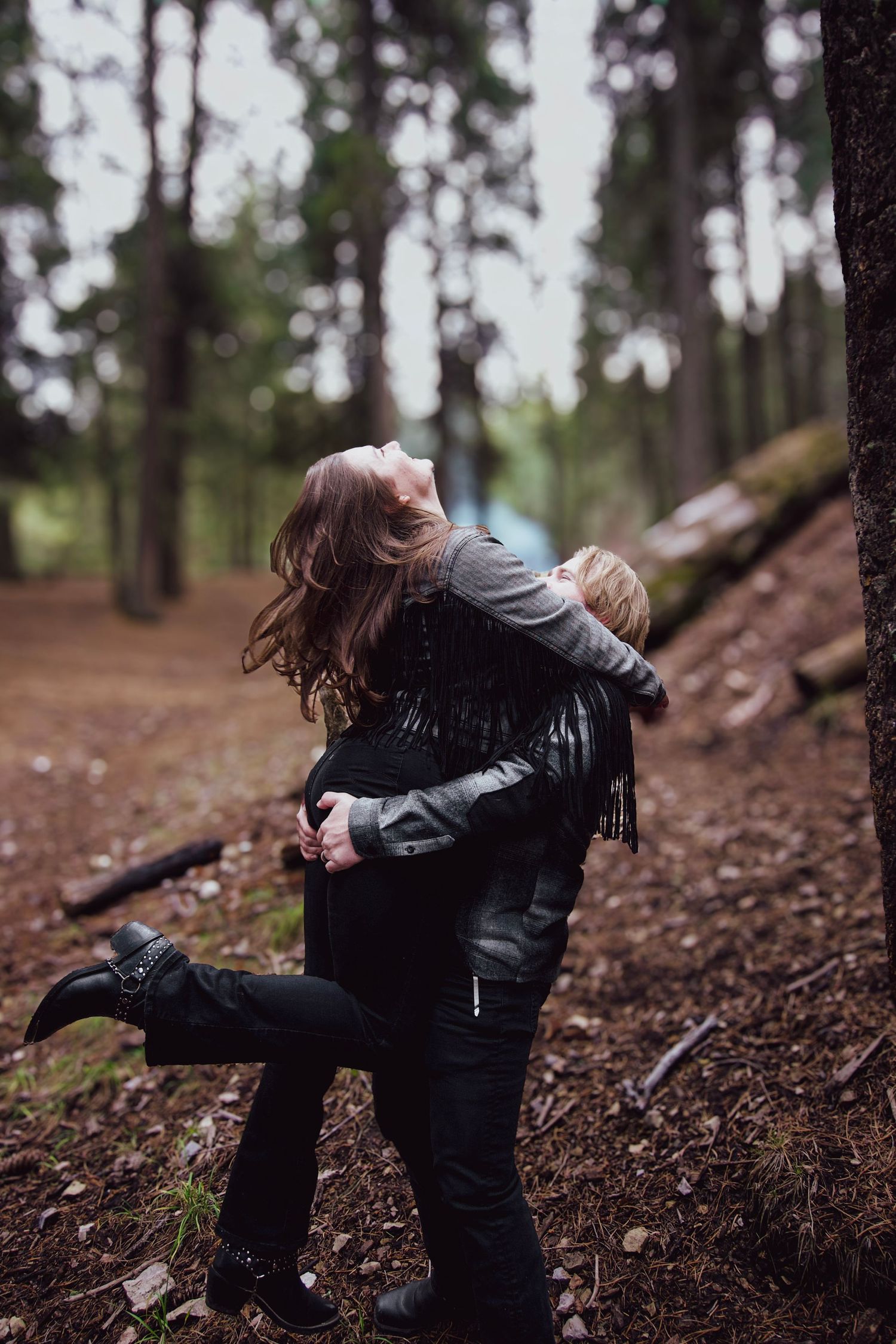 Two people in black clothing share a playful moment in a moody forest setting.