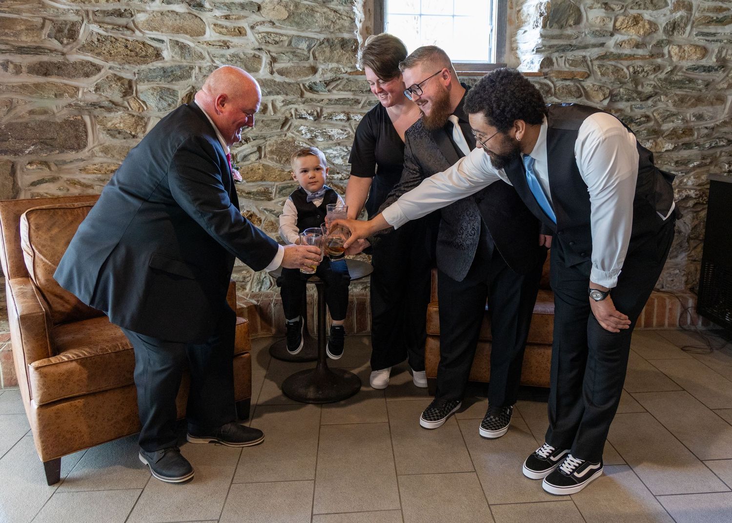 Group of groomsmen bent over looking at something interesting on the stone floor of a rustic venue.