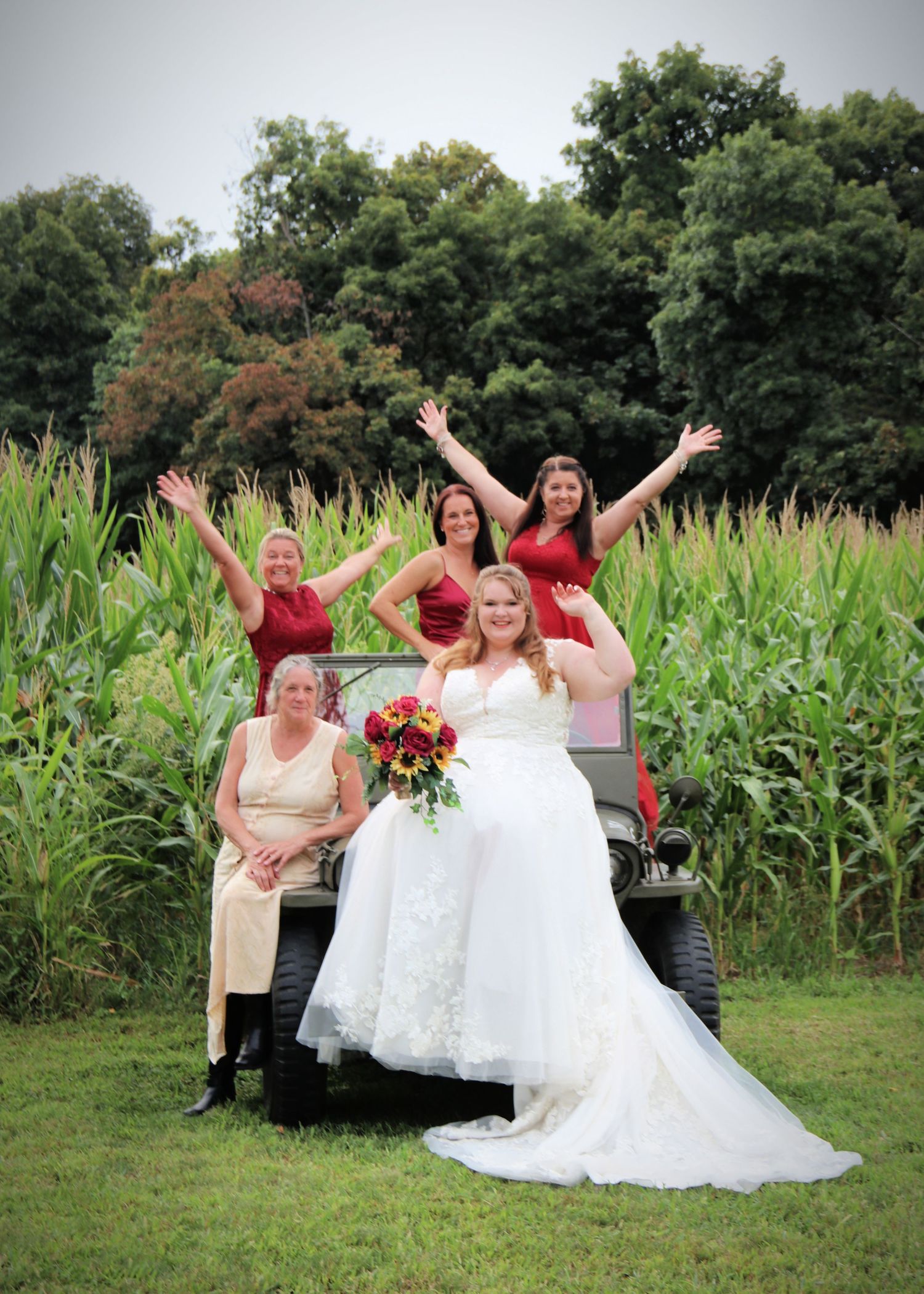Group celebrating in front of cornfield with a golf cart during outdoor wedding festivities.