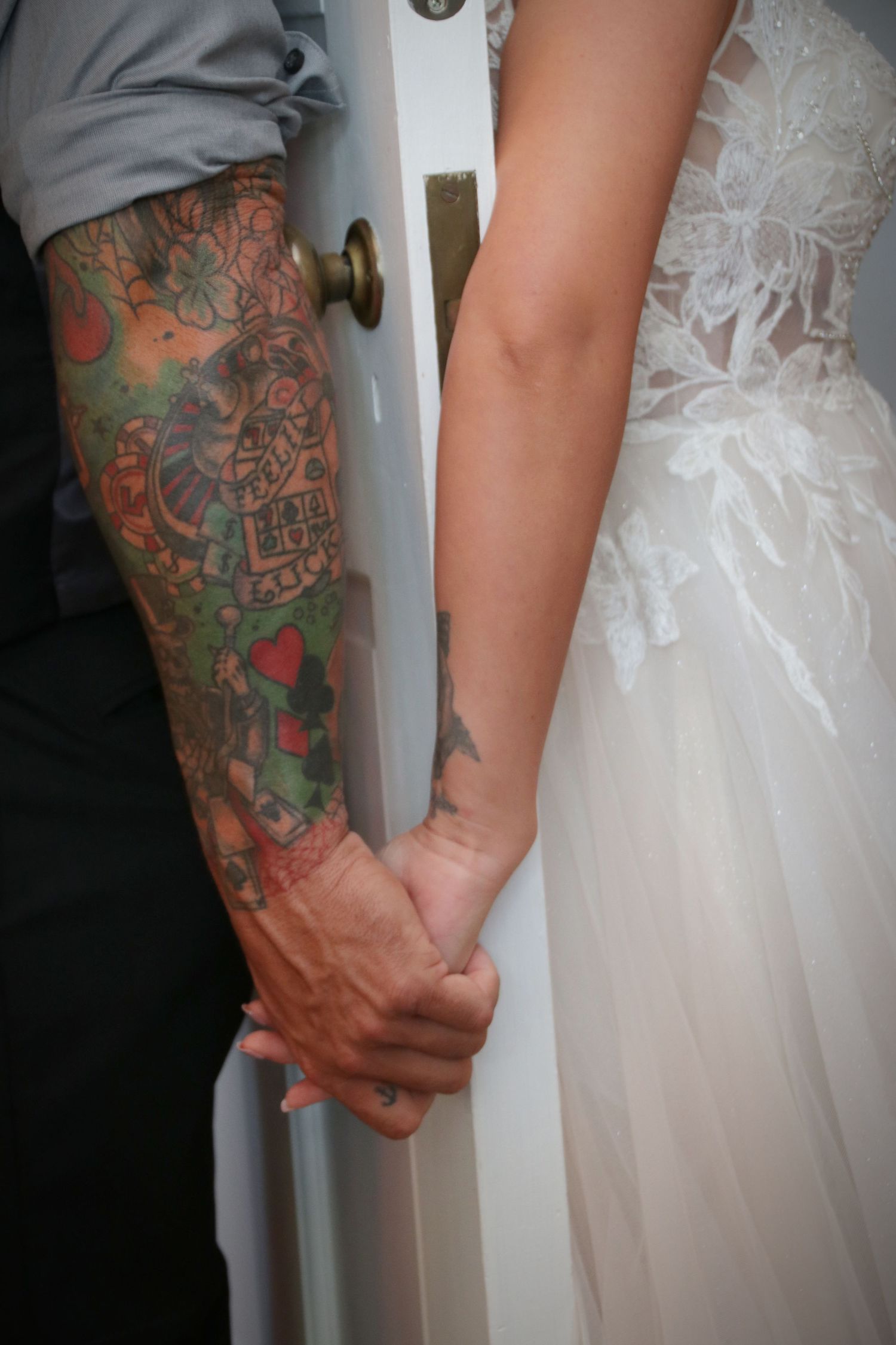 Close-up of tattooed arm holding hands with someone wearing a white wedding dress.