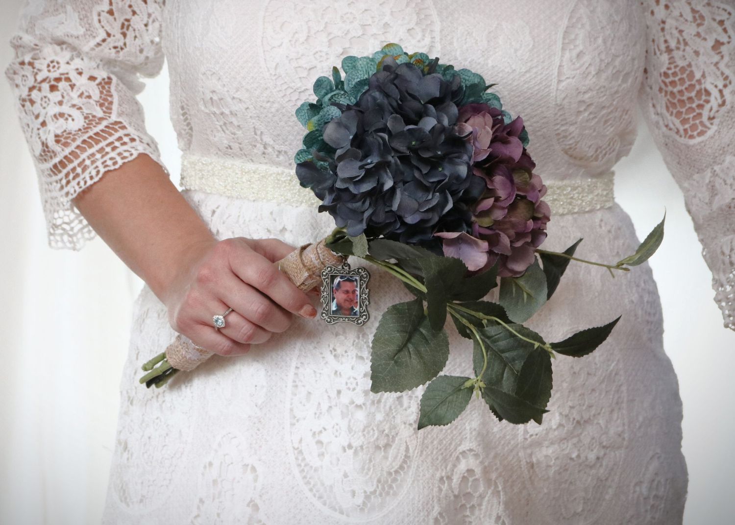 Close up of lace wedding dress detail with blue and purple hydrangea bouquet.