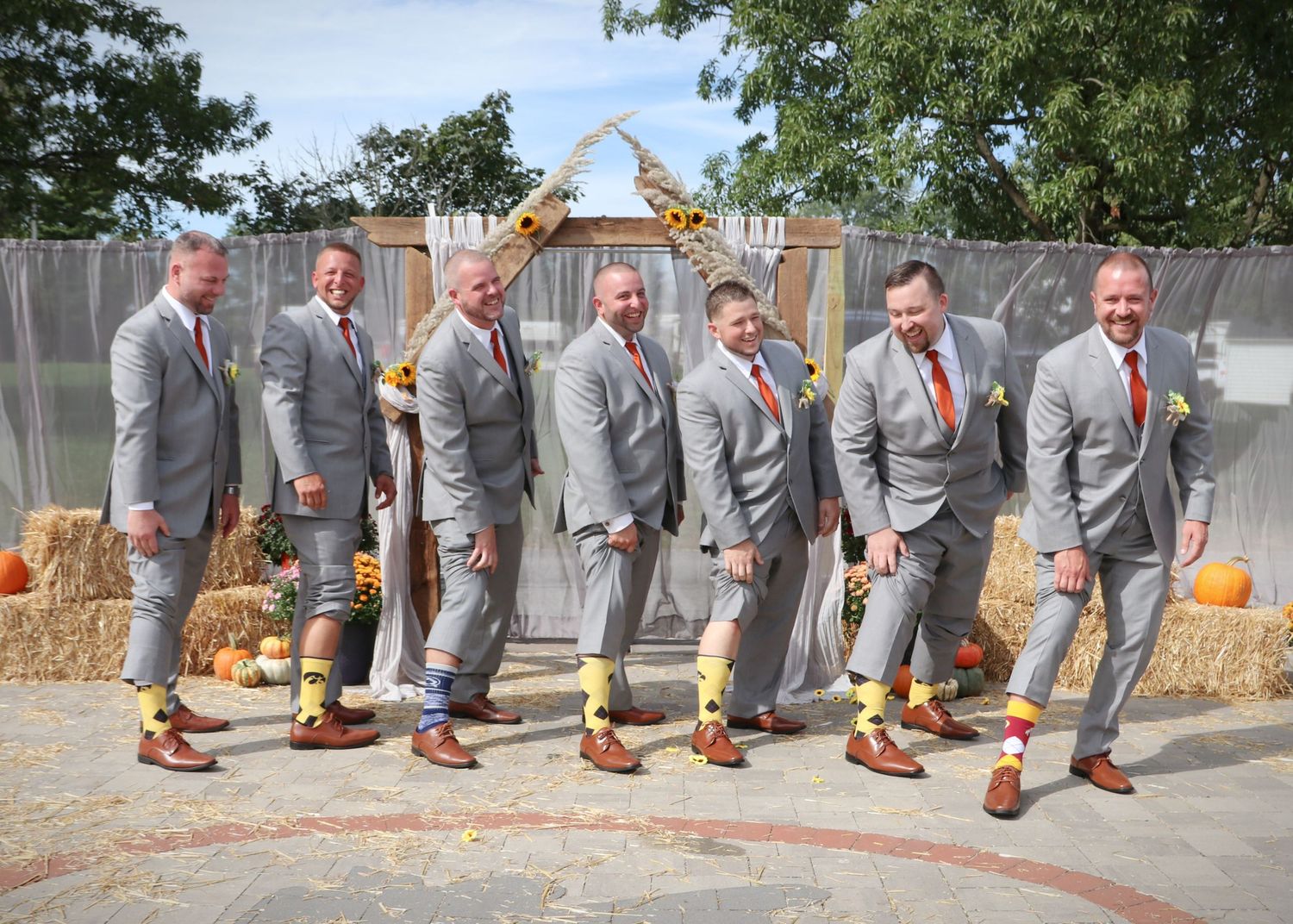 Groomsmen in matching gray suits and red ties pose playfully in a line outdoors.