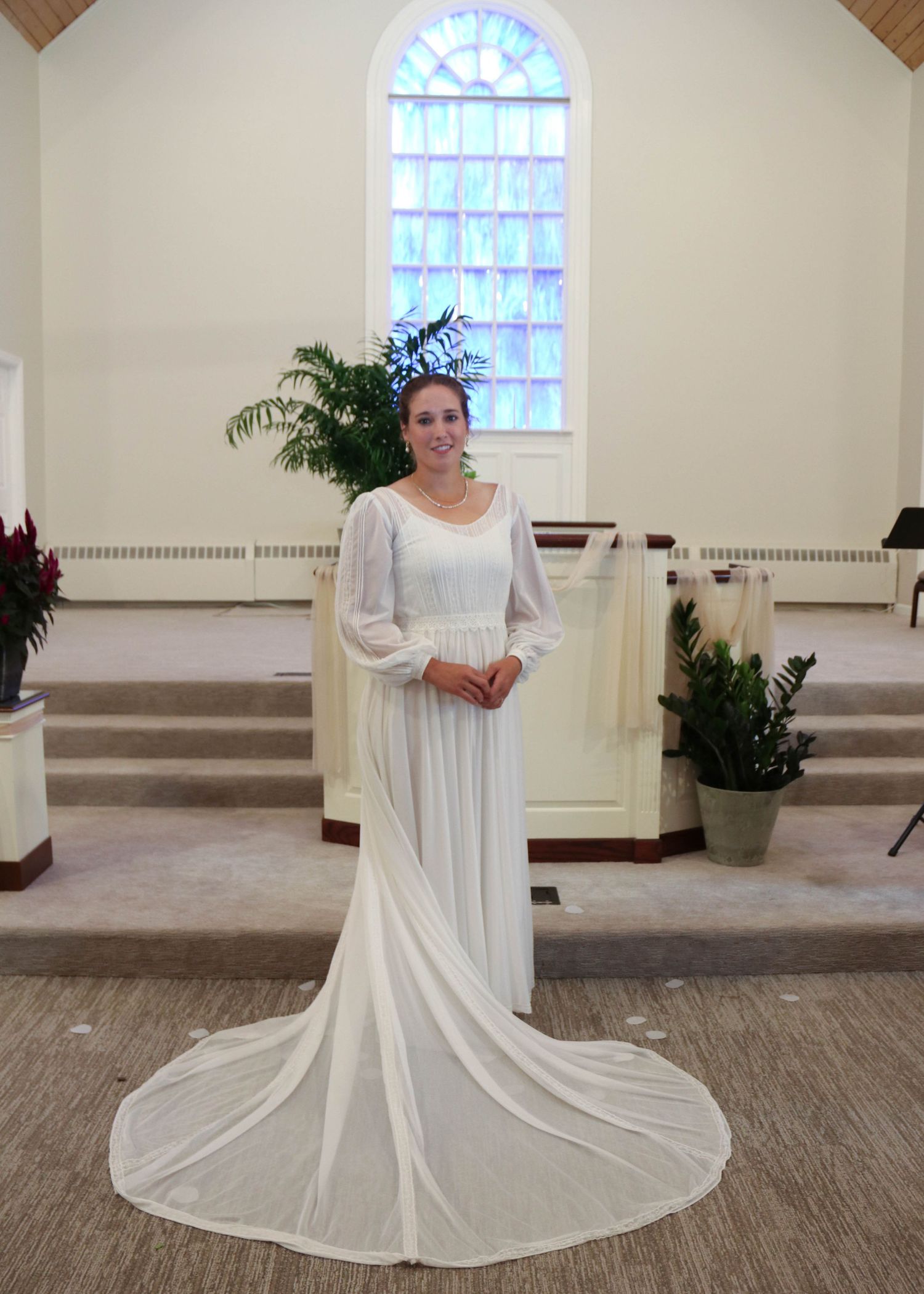 Long white wedding dress with train photographed in church setting with stained glass window.