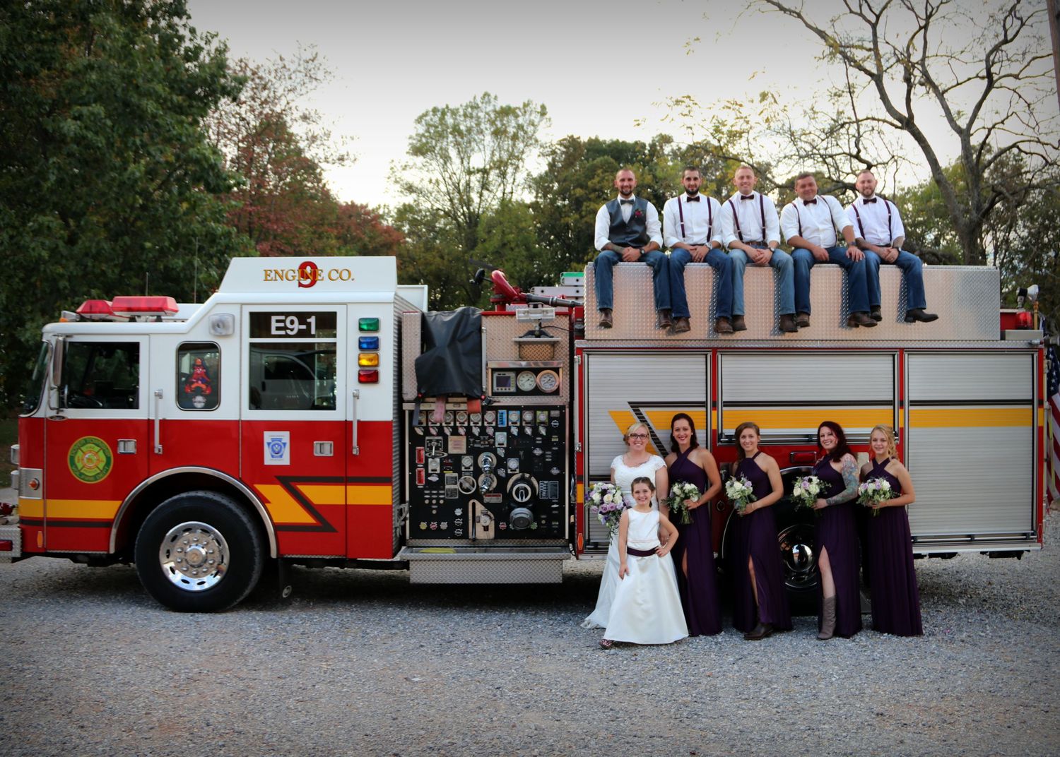 Wedding party poses creatively on a red fire truck for unique group photo.