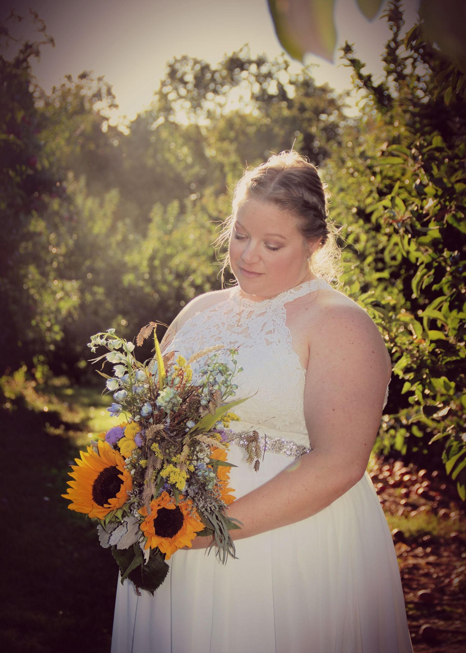 A romantic bridal portrait in a garden setting featuring a white lace dress and vibrant sunflower bouquet.