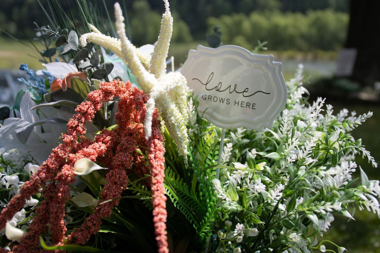 Rustic floral arrangement with coral and white flowers against a sunlit garden backdrop.