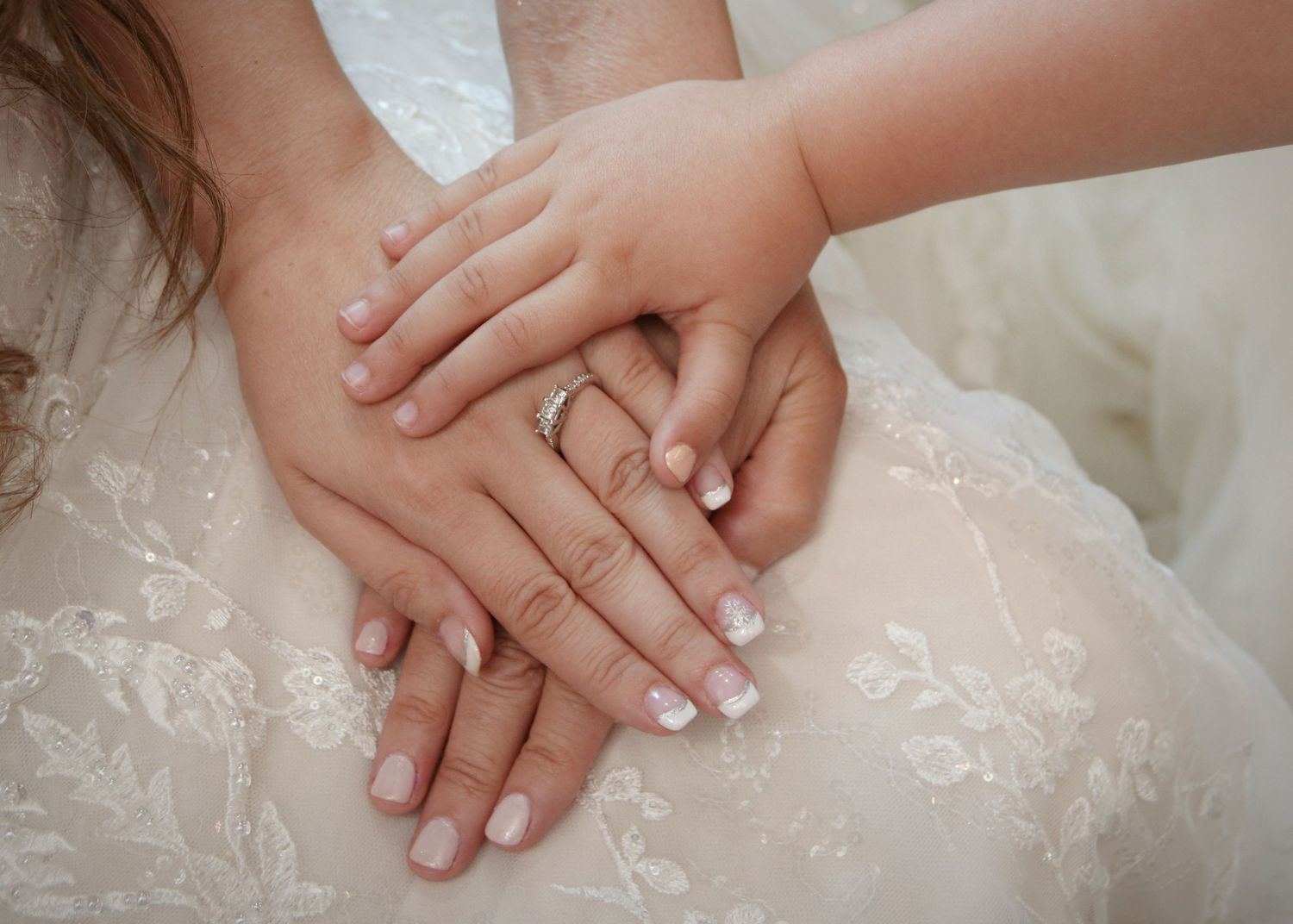 Close-up of hands with wedding rings stacked together on white lace fabric.