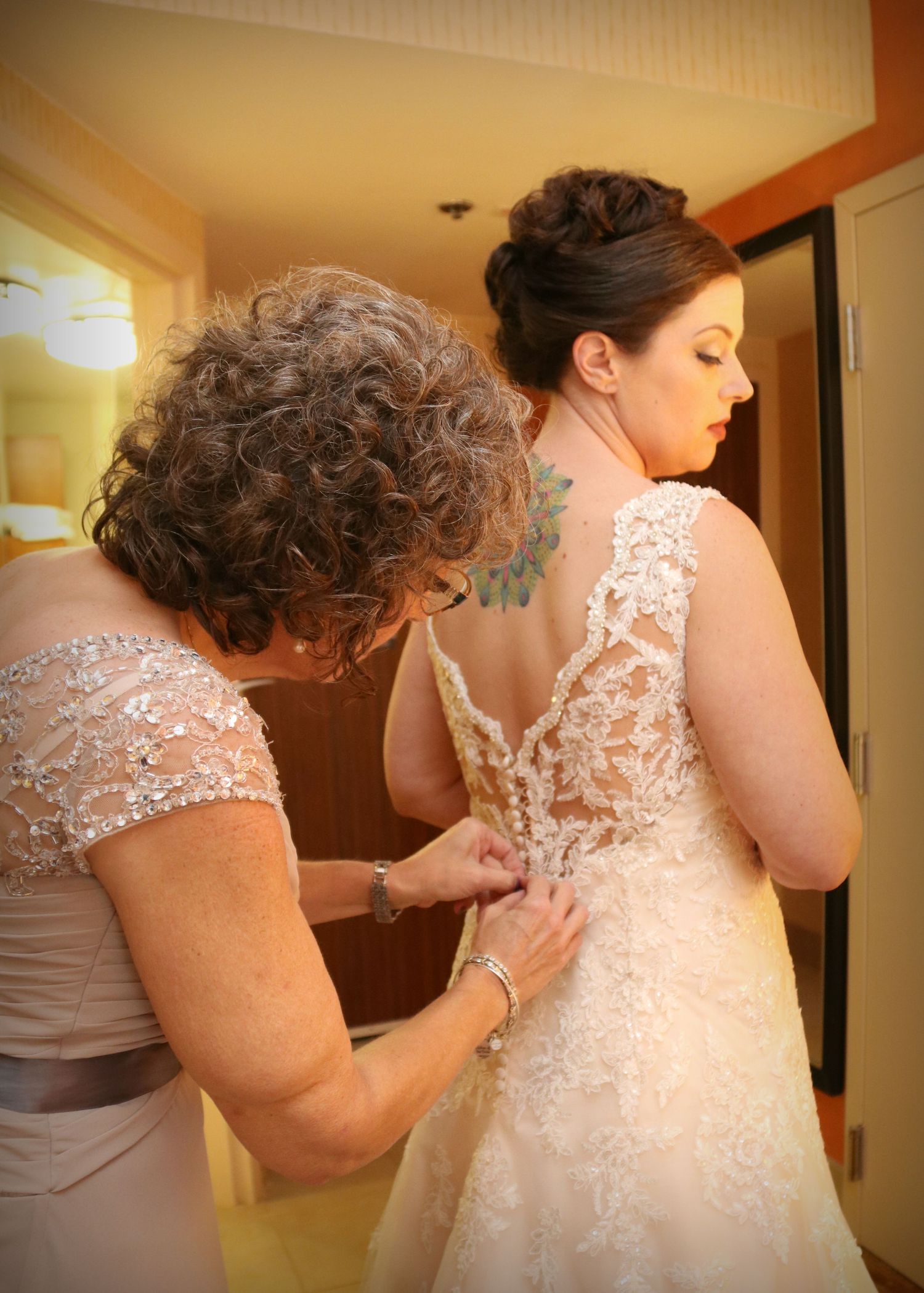 A delicate lace wedding dress is being buttoned up during the getting ready process.