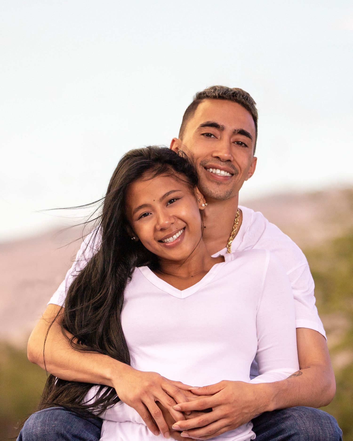 Couple in white shirts embracing outdoors during golden hour portrait session.