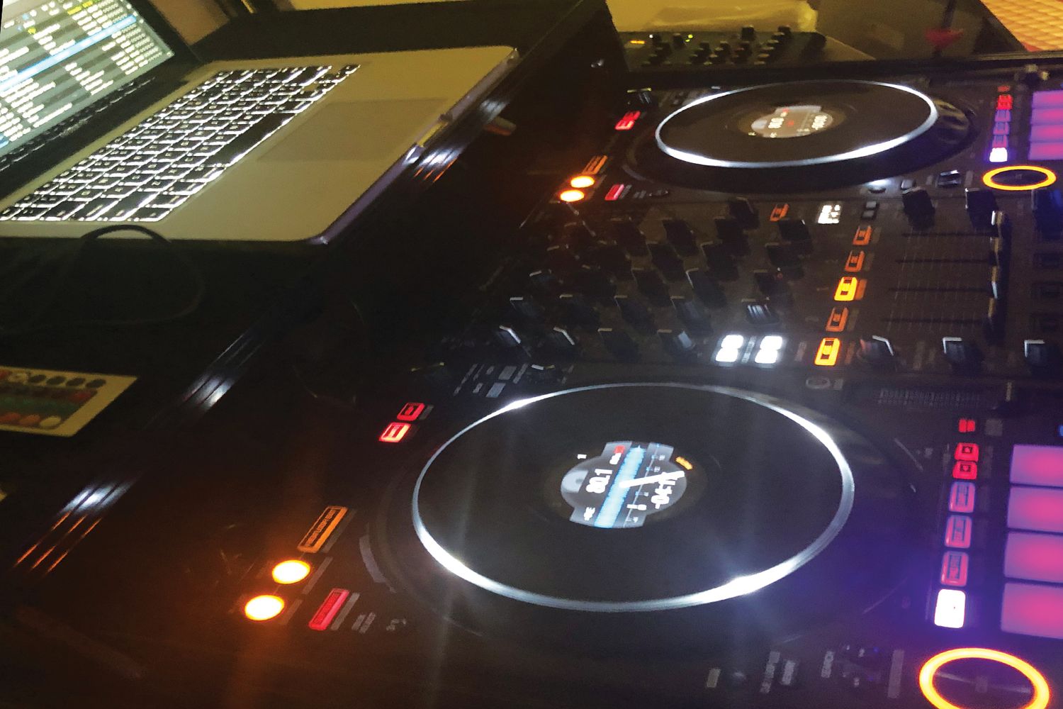 DJ controller setup with illuminated turntables and laptop for music mixing.
