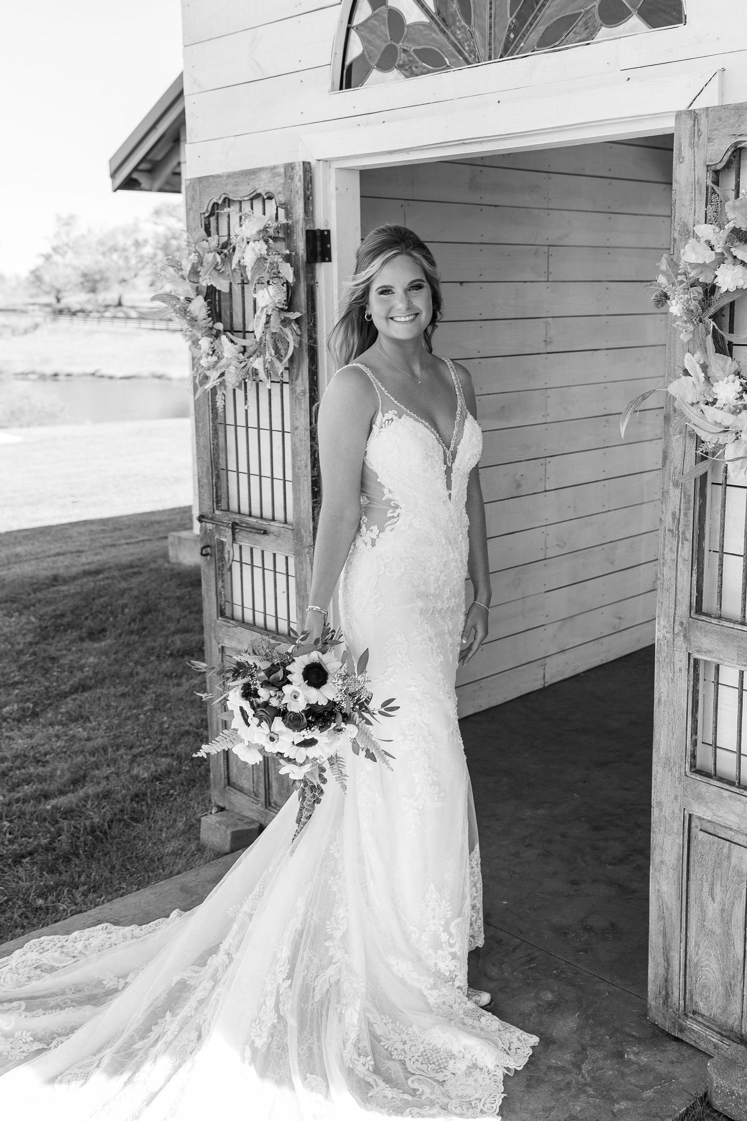 Elegant lace wedding gown with train photographed against rustic white chapel backdrop.