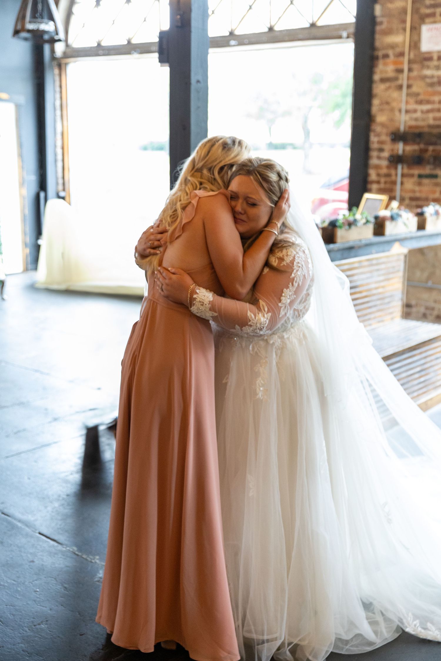 An emotional embrace shared between a bride in white and bridesmaid in blush pink.