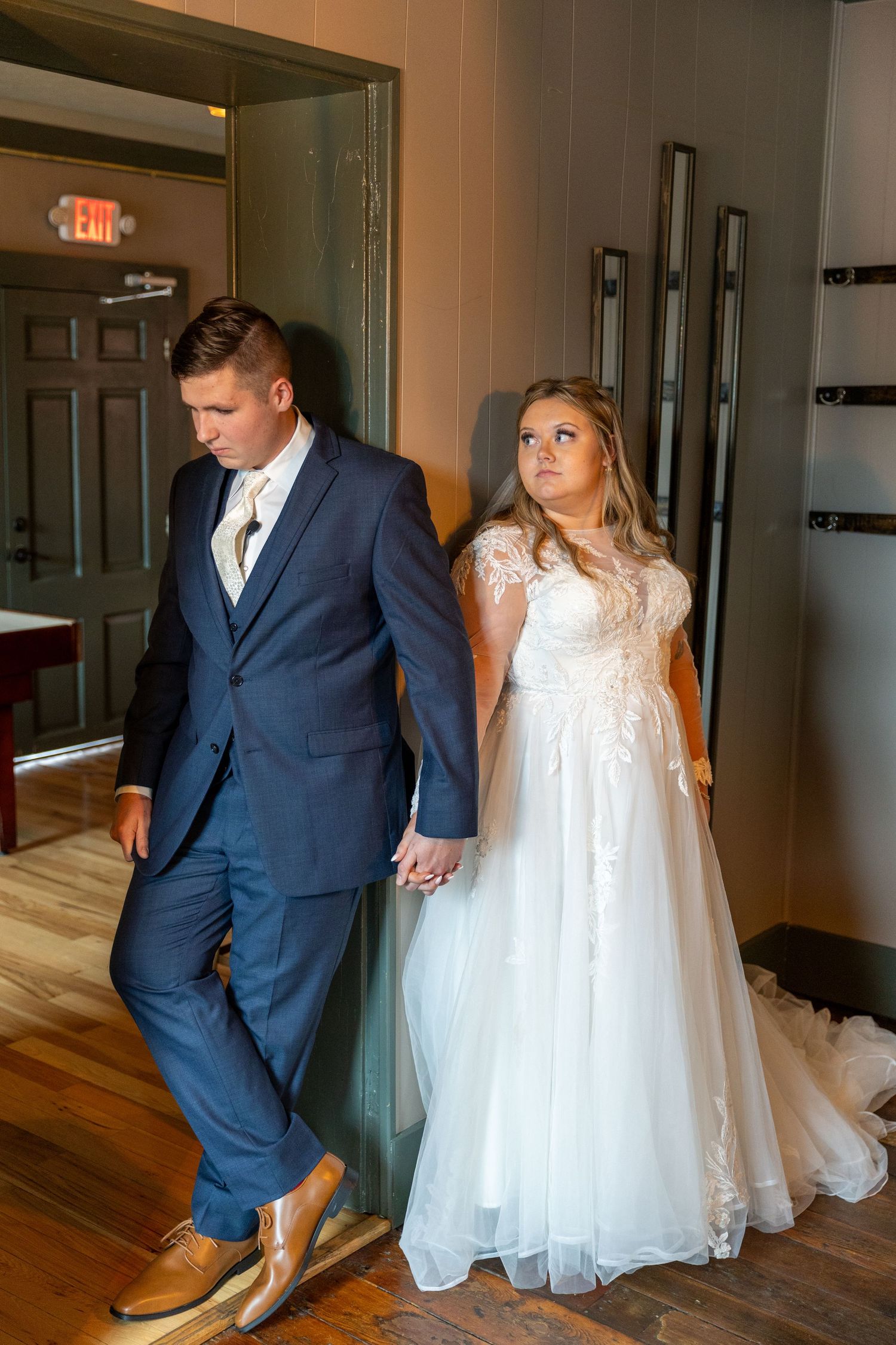 A couple stands in a hallway wearing wedding attire before their ceremony.