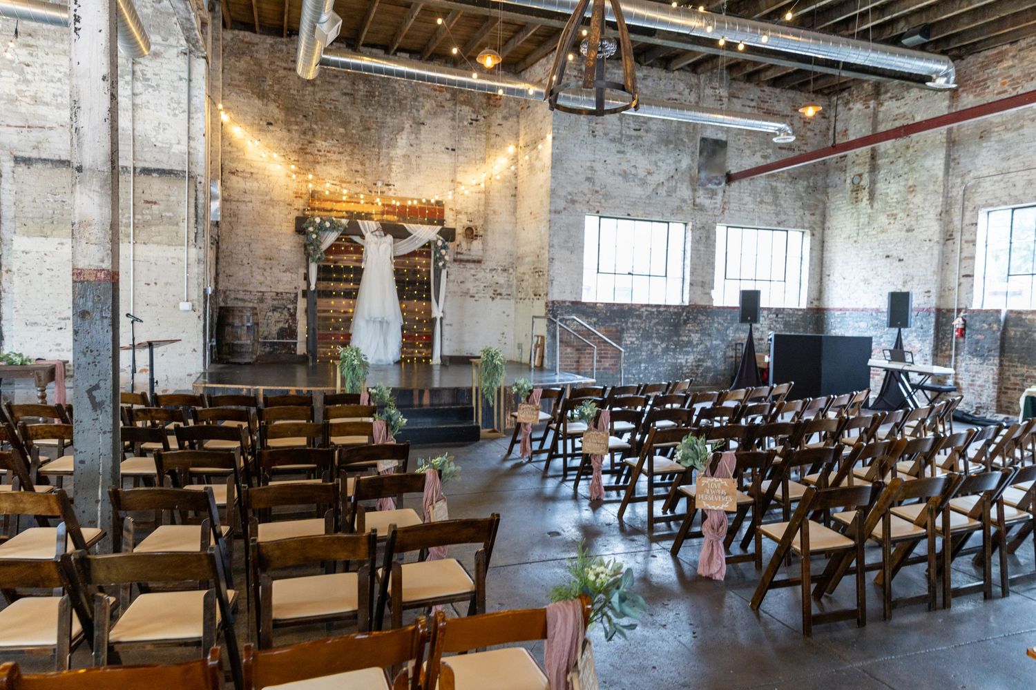 Industrial style wedding ceremony venue with exposed brick walls and wooden chairs.