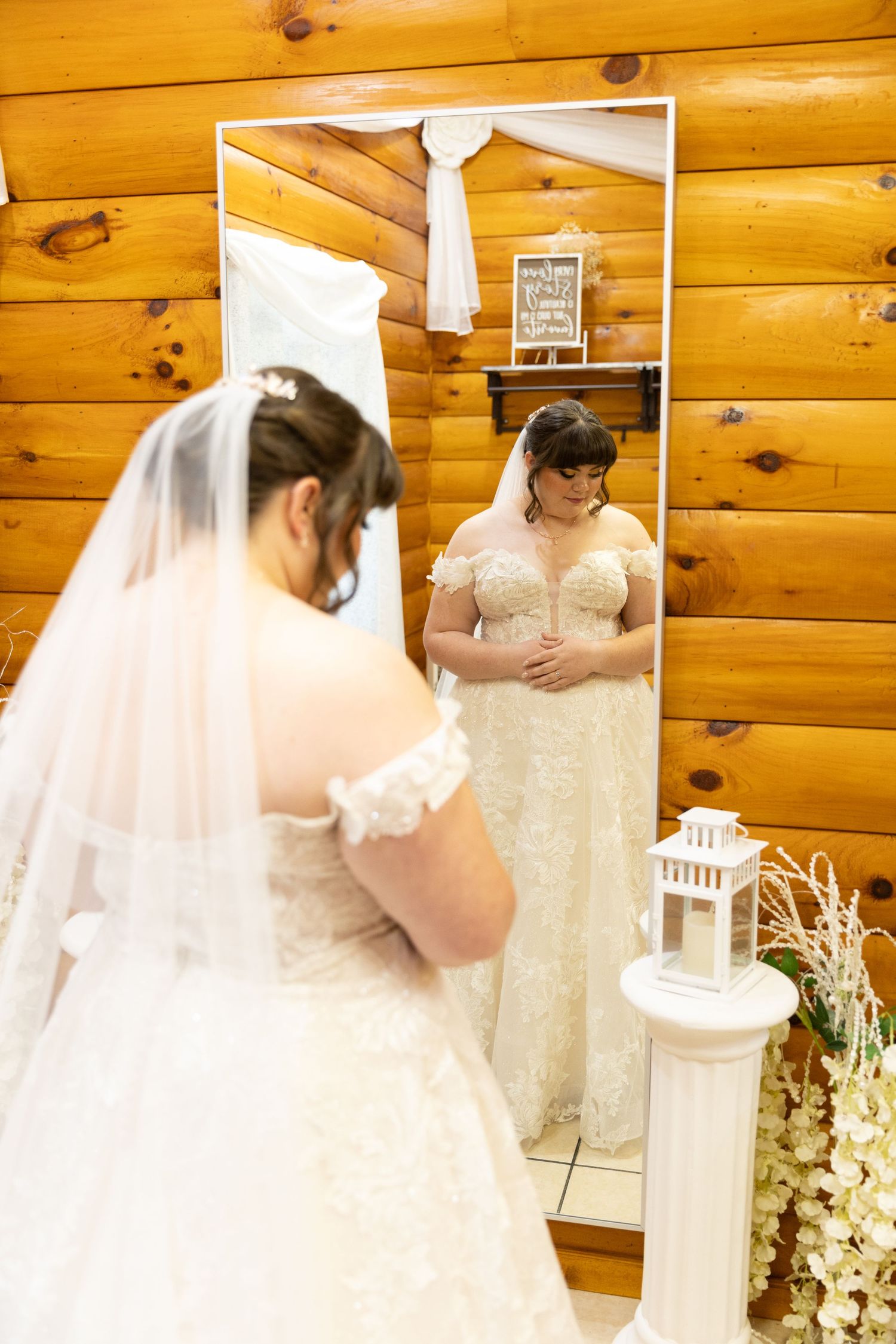 A wedding dress and white tie displayed in a rustic wooden room with decorative lanterns.