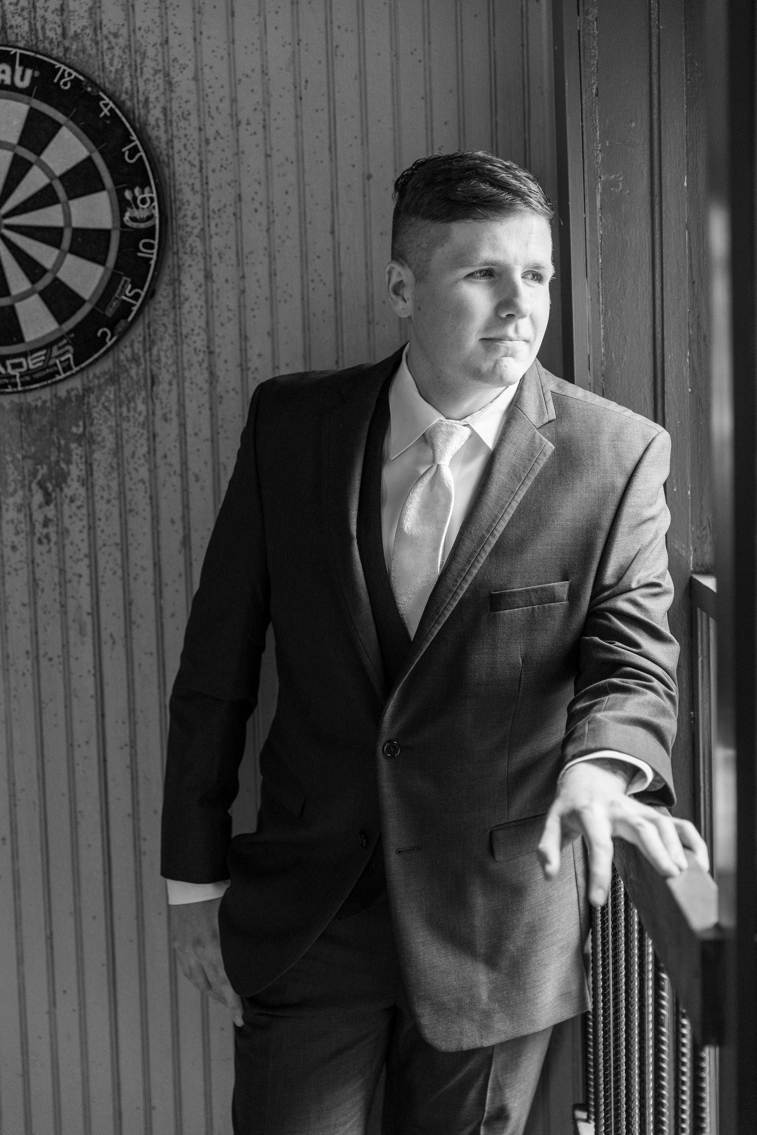 Black and white portrait of suited figure near dartboard in classic pose.