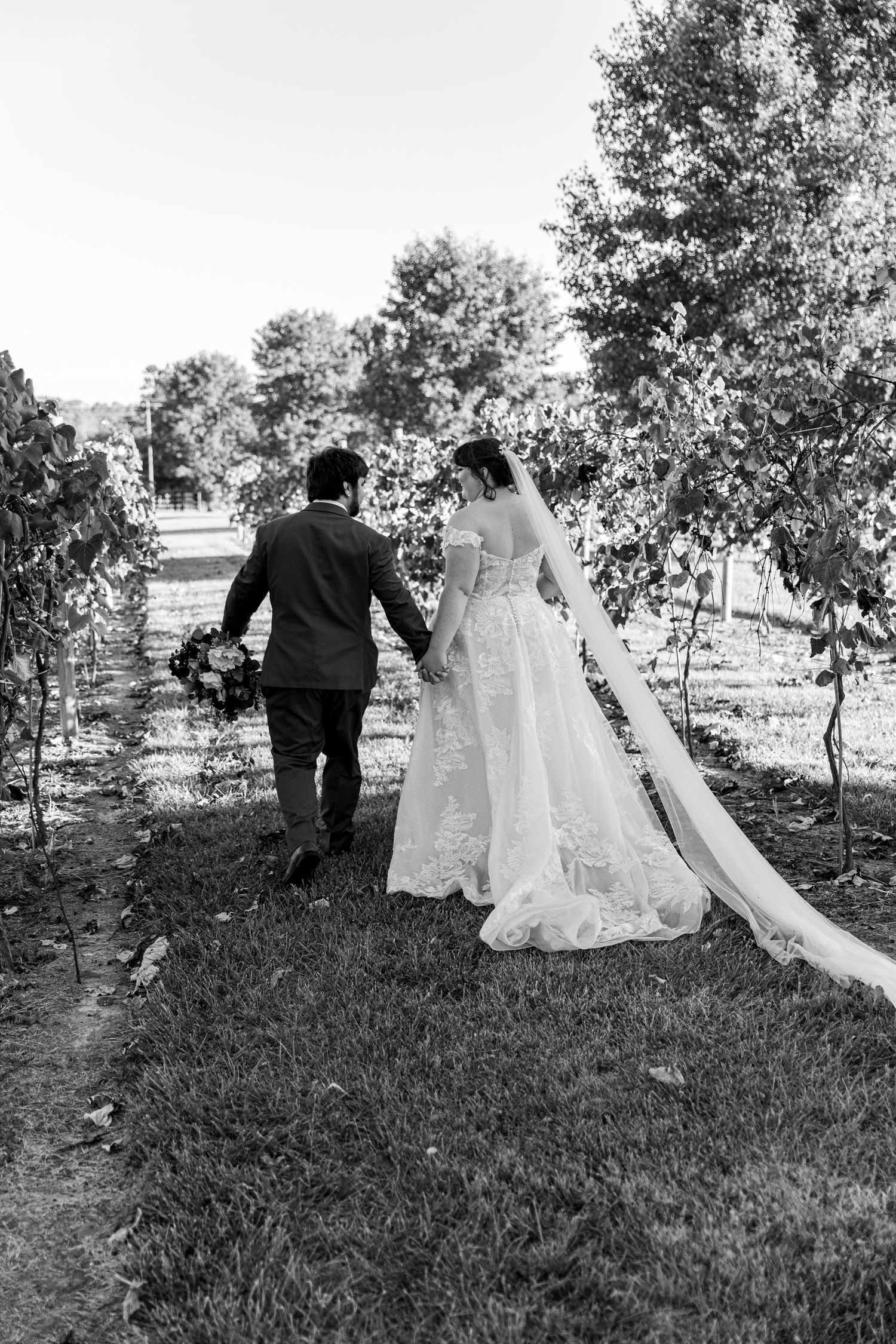A romantic black and white photo of newlyweds walking through a garden path.