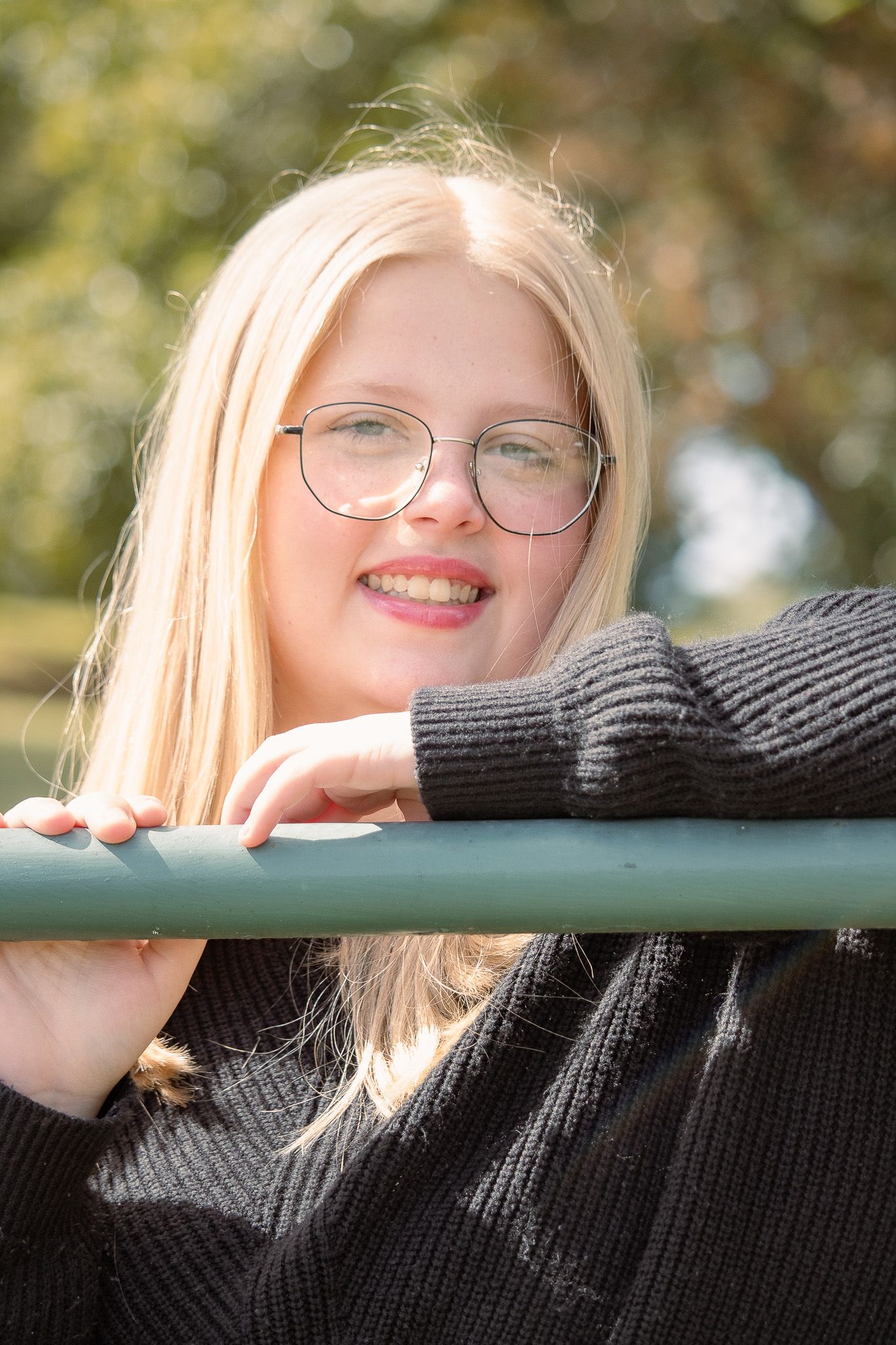 Portrait of a person with glasses leaning on a railing in soft natural lighting.