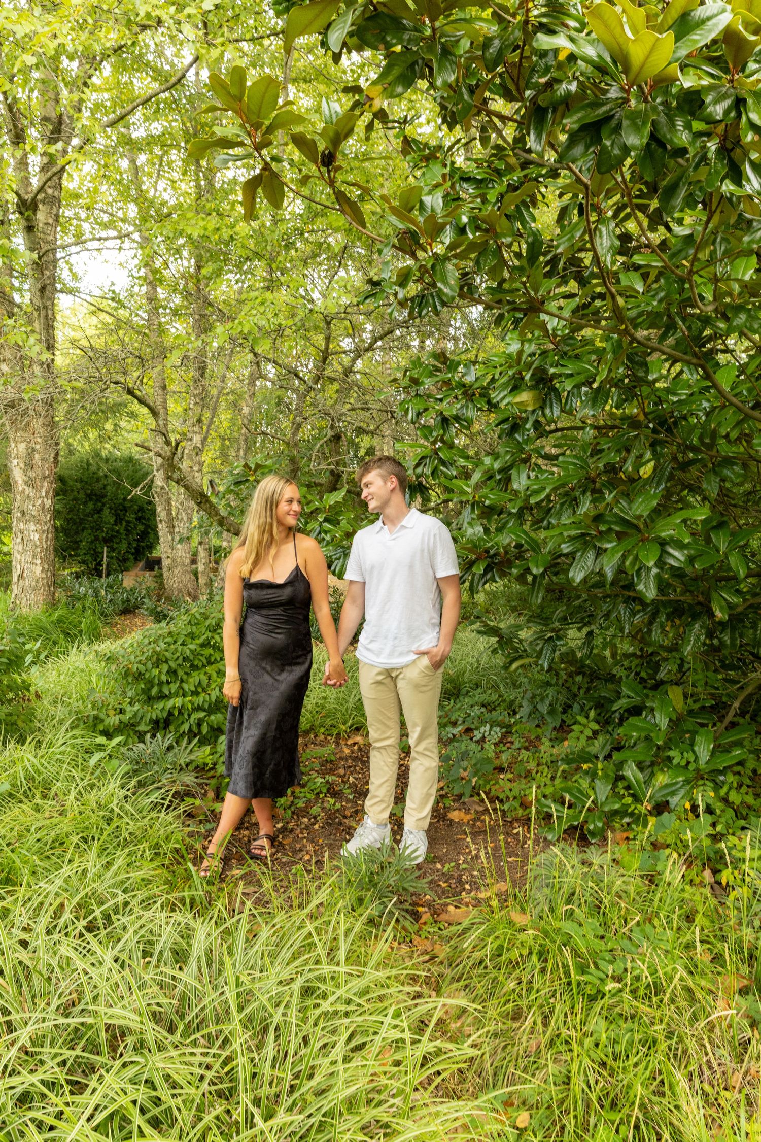 Couple walks hand in hand through a lush garden pathway surrounded by magnolia trees.