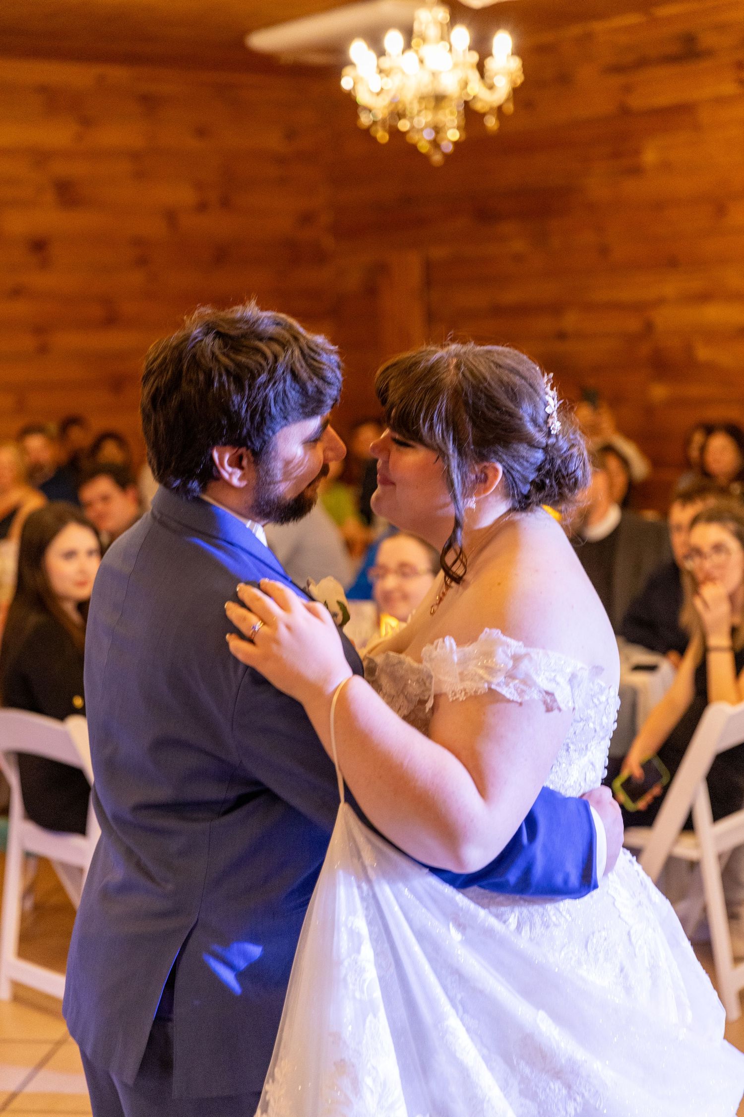 A couple shares their first dance under a warm chandelier at their wedding reception.